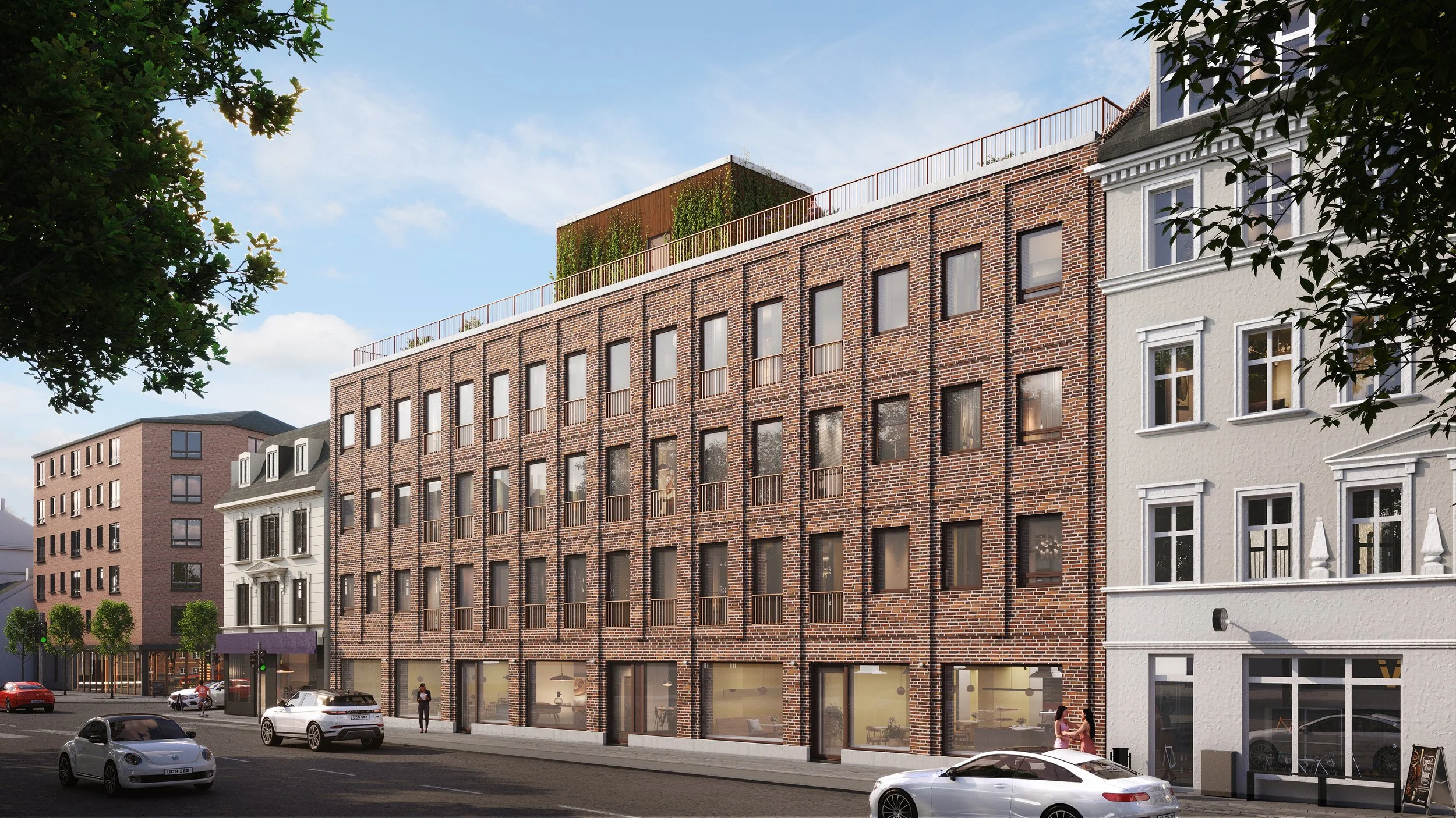 Kunstnerisk gengivelse af en moderne bygningsfacade med røde mursten, store vinduer og en tagterrasse med grønne planter, omgivet af ældre og moderne bygninger, biler på vejen og fodgængere på fortovet.