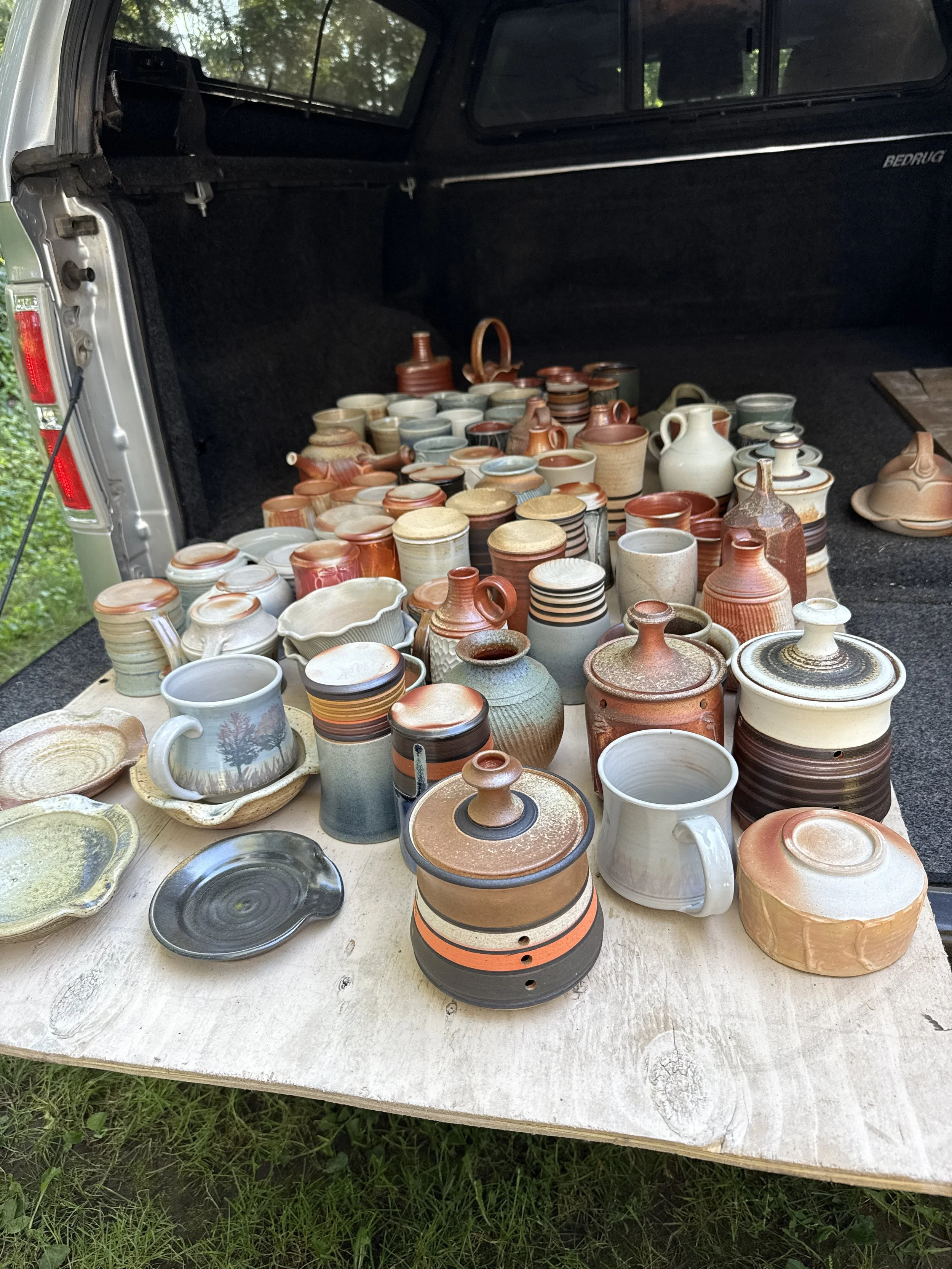 Freshly fired collection of handmade pottery, including bowls, cups, vases, and teapots, tumblers, garlic jars displayed on a wooden table.