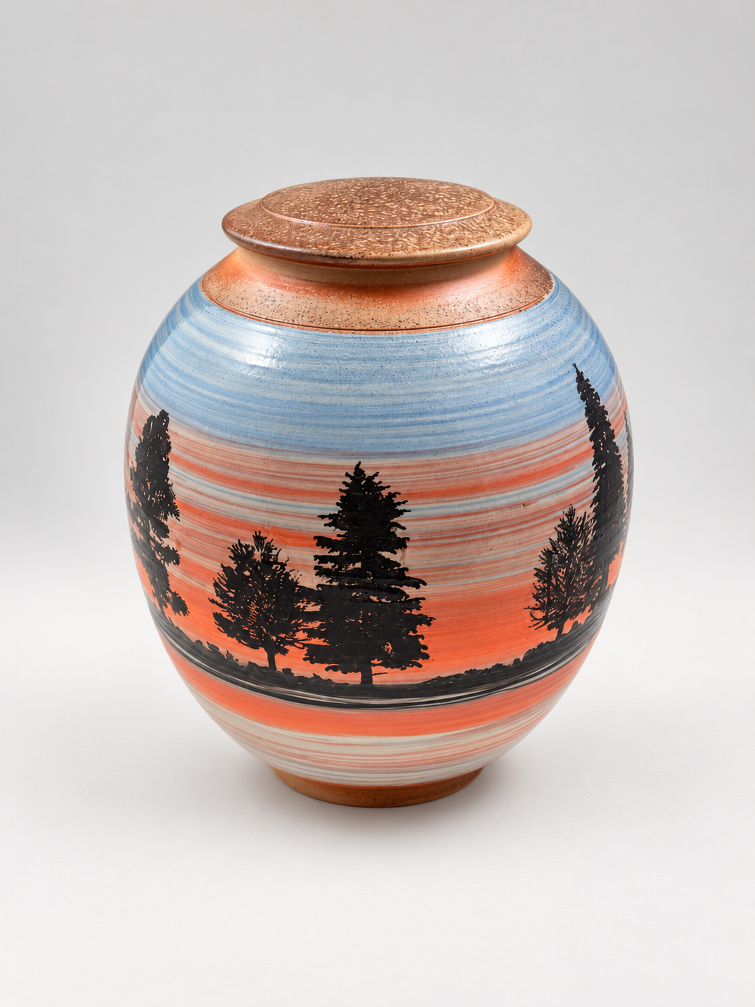 Handcrafted lidded stoneware jar featuring silhouetted pine trees against a blue and coral sunset landscape. One-of-a-kind pottery by Chad Jerzak.