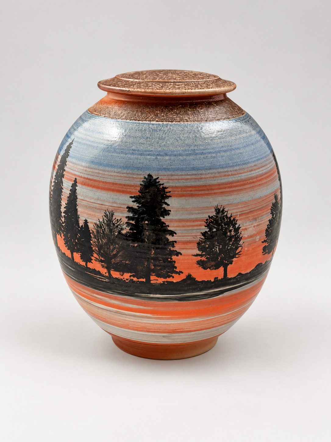 Handcrafted lidded stoneware jar featuring silhouetted pine trees against a blue and coral sunset landscape. One-of-a-kind pottery by Chad Jerzak.