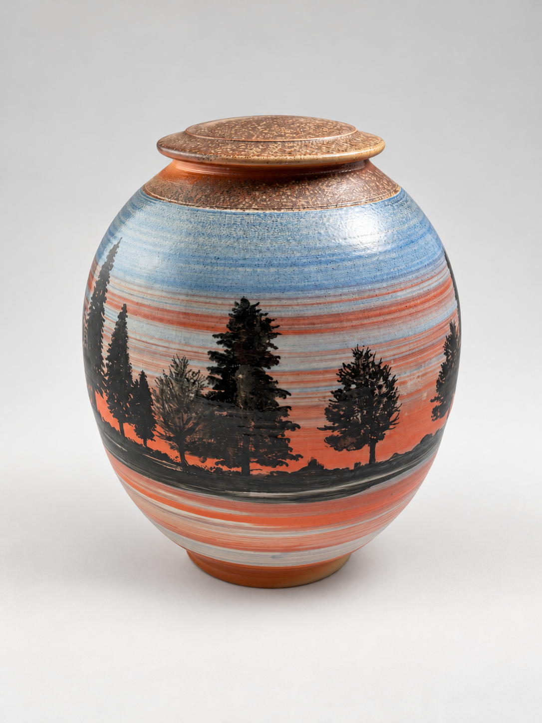 Handcrafted lidded stoneware jar featuring silhouetted pine trees against a blue and coral sunset landscape. One-of-a-kind pottery by Chad Jerzak.