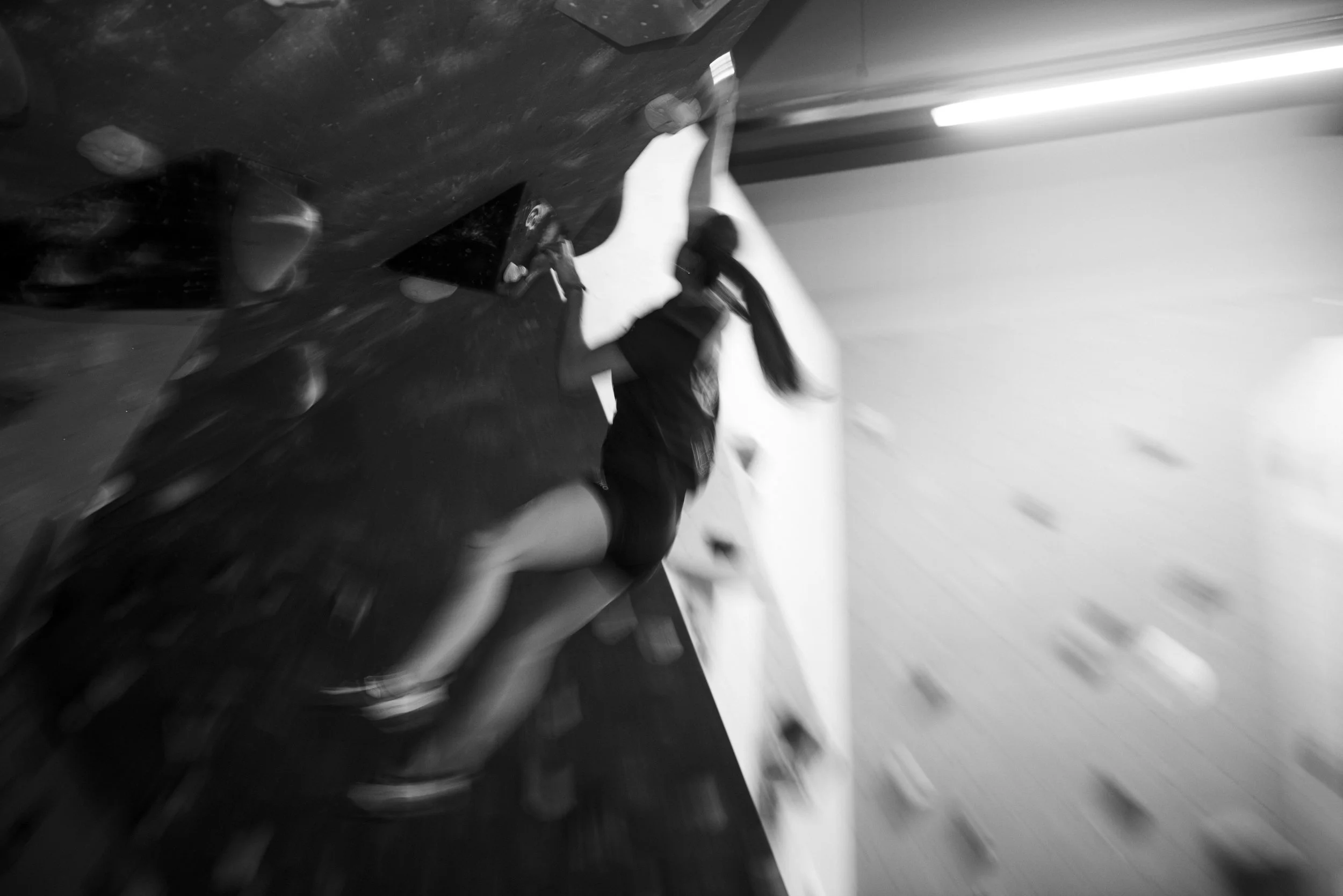 Een jonge vrouw die klimt op een binnenmuur voor rotsklimmen, gefocust op haar handgrepen.