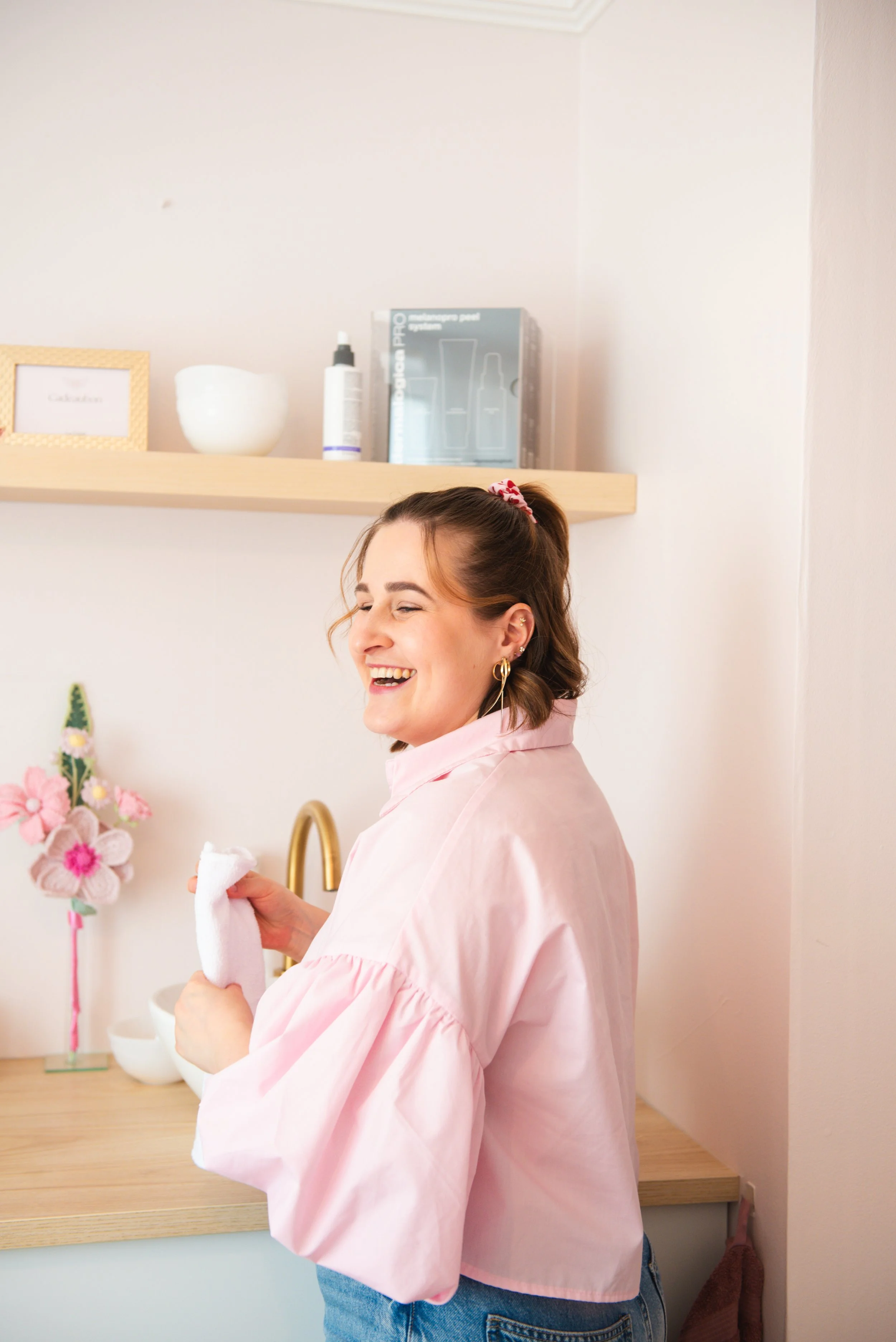 Vrouw die lacht en een handdoek vasthoudt in een moderne, lichte keuken met bloemen en een goudkleurige kraan.
