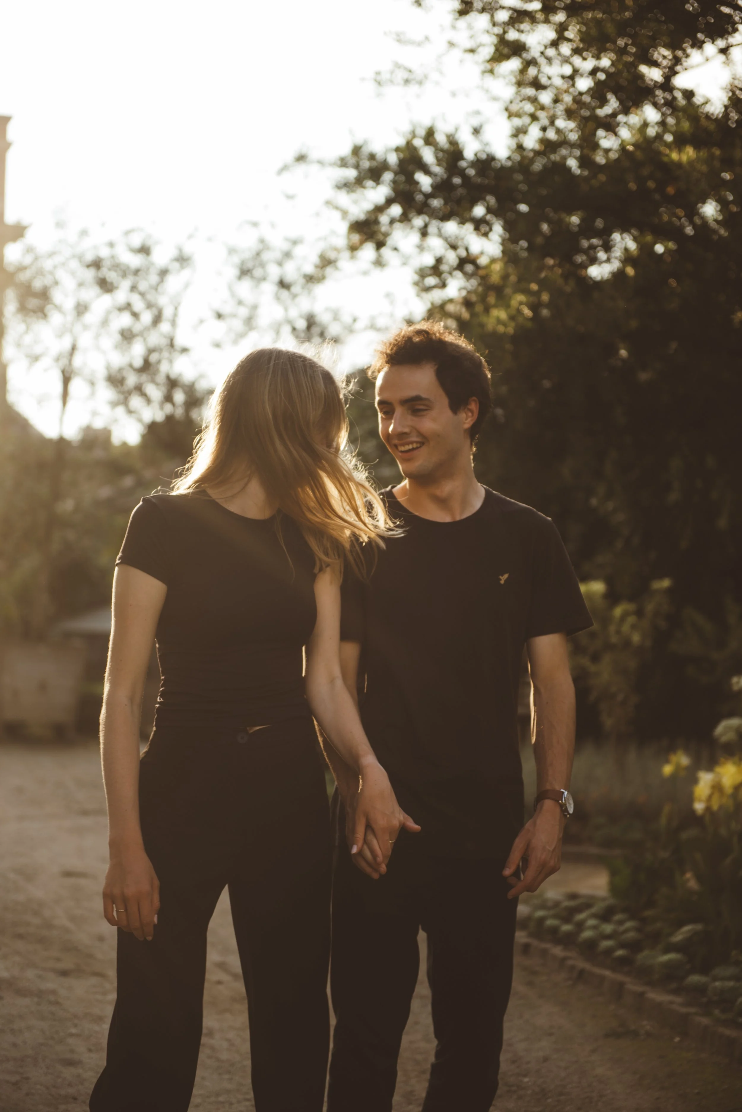 Een koppel houdt elkaars handen vast en loopt samen in een park tijdens zonsondergang.