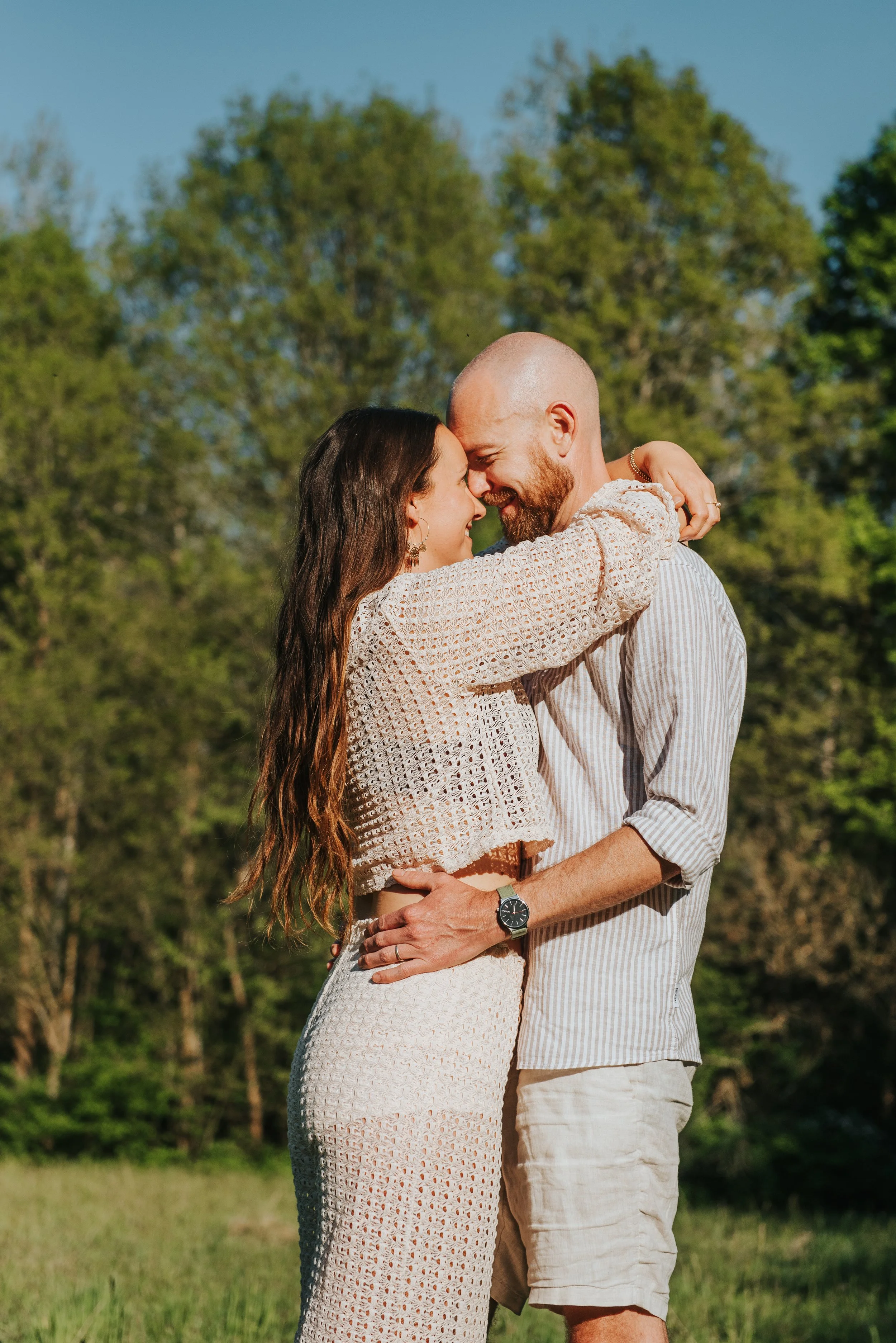 Een liefdeskoppeltje omhelst elkaar in een groene buitenomgeving op een zonnige dag.