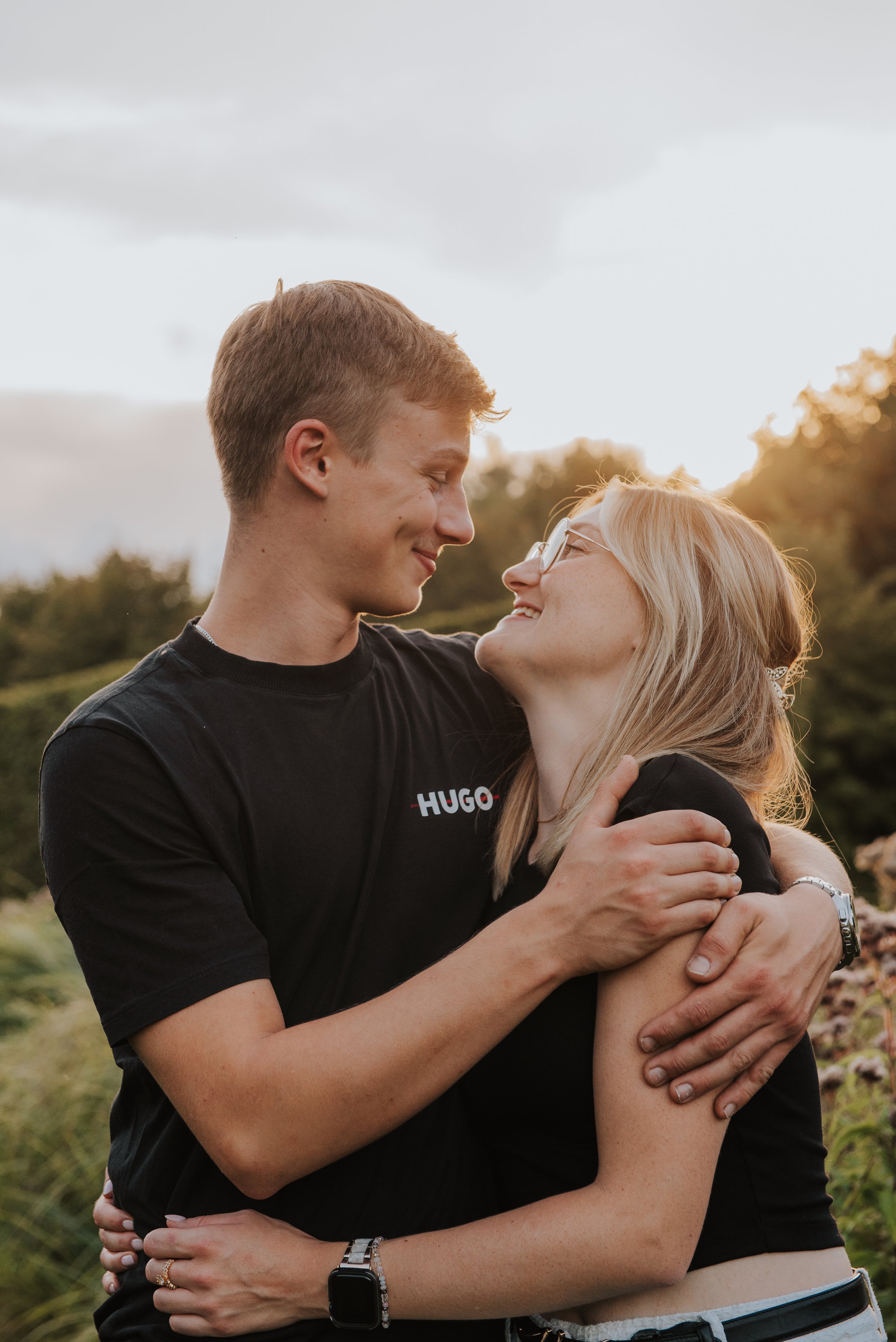 Een jongeman en een jongedame die elkaar liefdevol omarmen in een buitenomgeving tijdens zonsondergang.