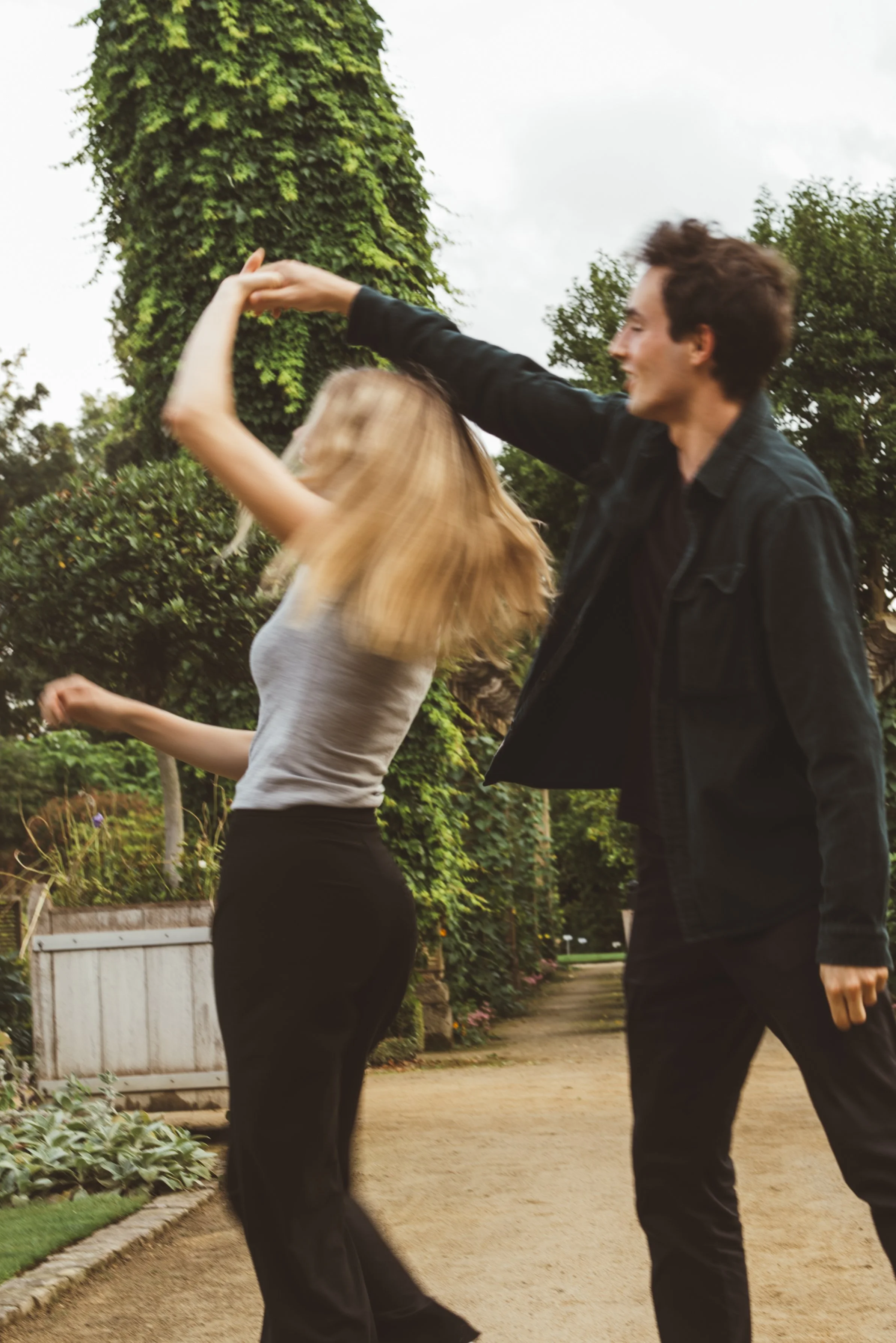Een man en een vrouw dansen samen buiten in een tuin, omringd door groen en struiken.