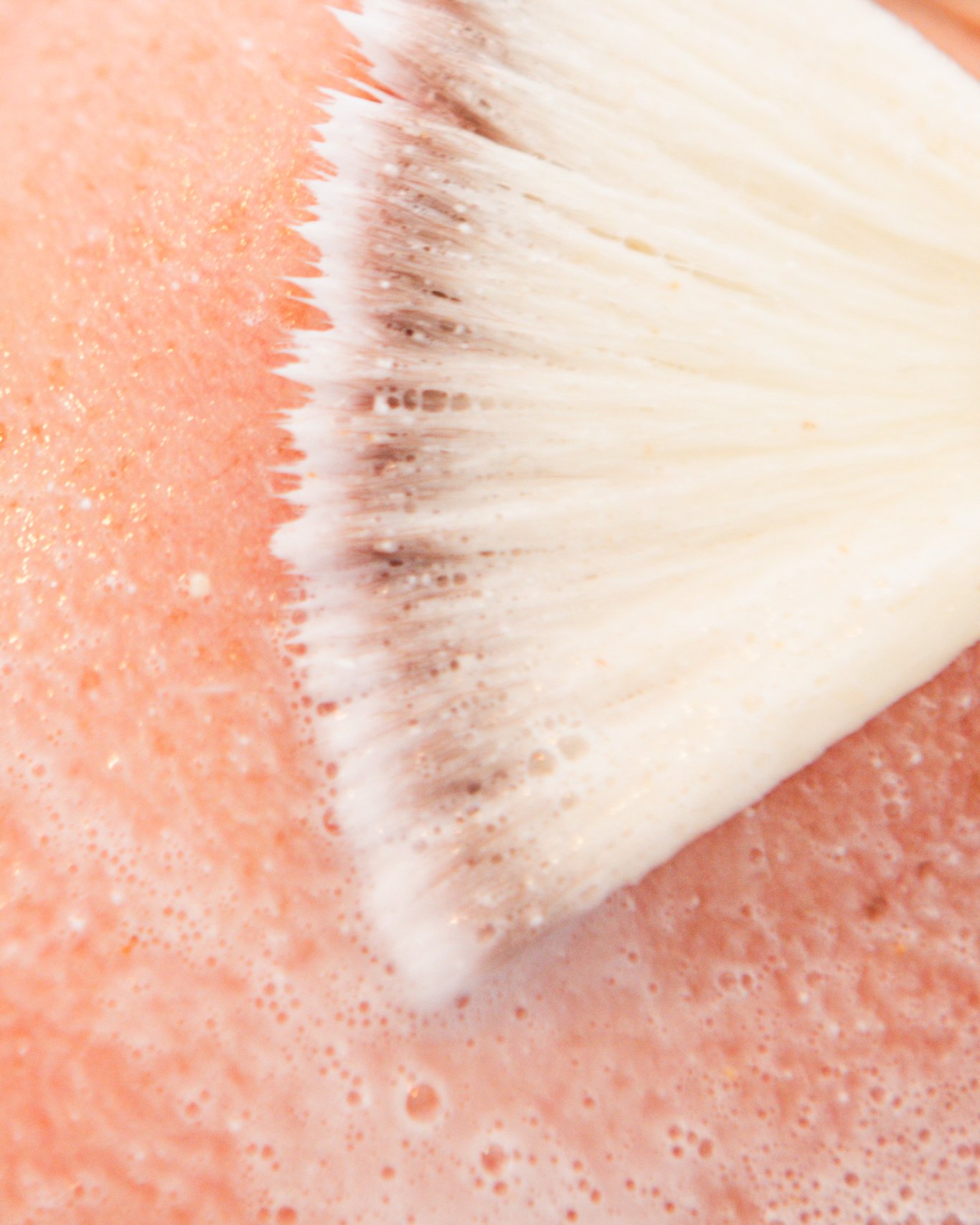 Close-up van een make-upborstel die over een gezicht met foundation wordt bewogen.