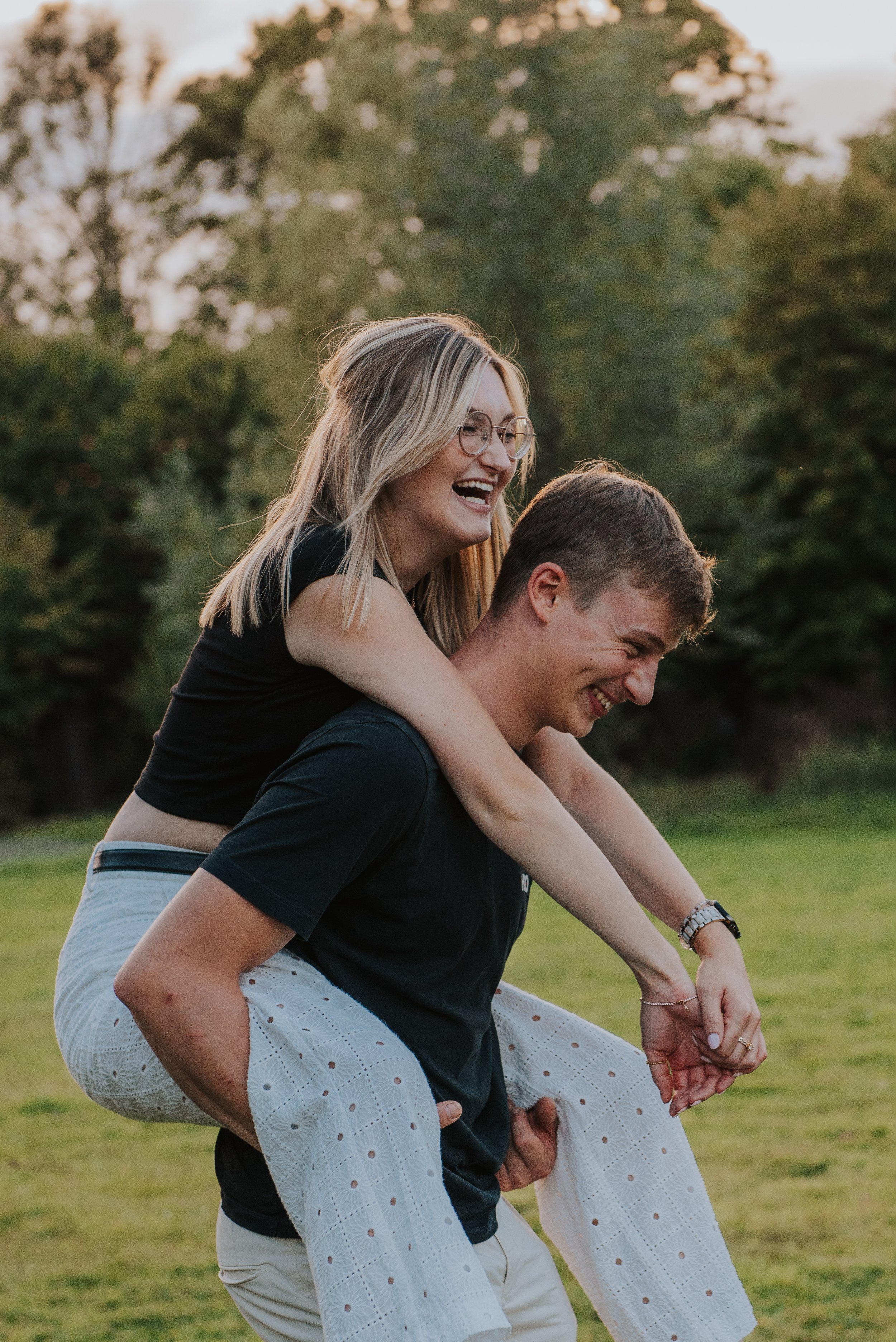 Twee jonge mensen lachen en hebben plezier samen in een groen park, de vrouw zit op de rug van de man terwijl ze plezier hebben.