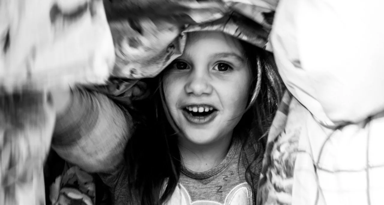 Een jonge meid kijkt door een open lapje of doek, glimlacht en heeft een blij gezicht.