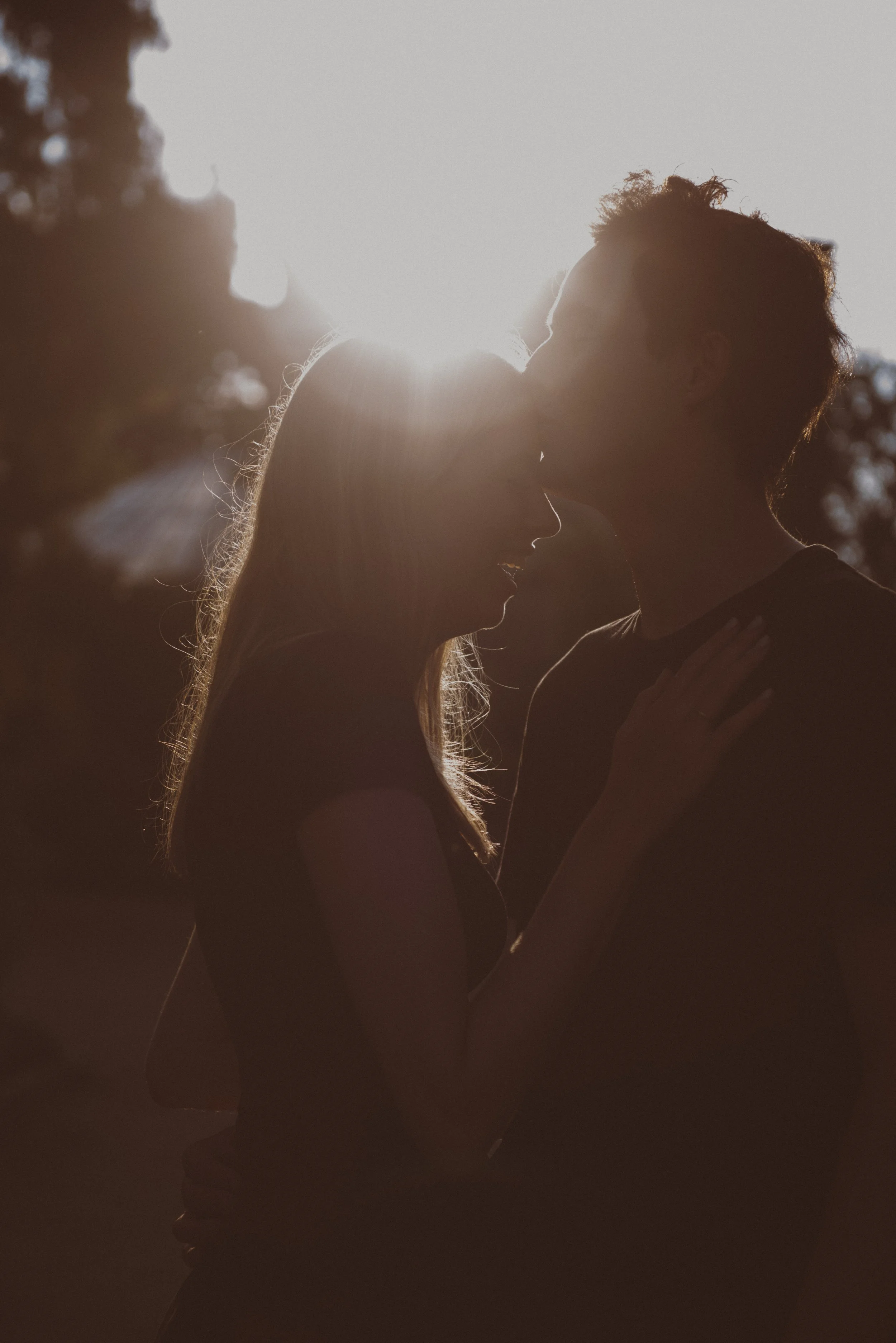 Een silhouet van een koppel dat elkaar kust bij zonsondergang, met de zon die op de achtergrond ondergaat.