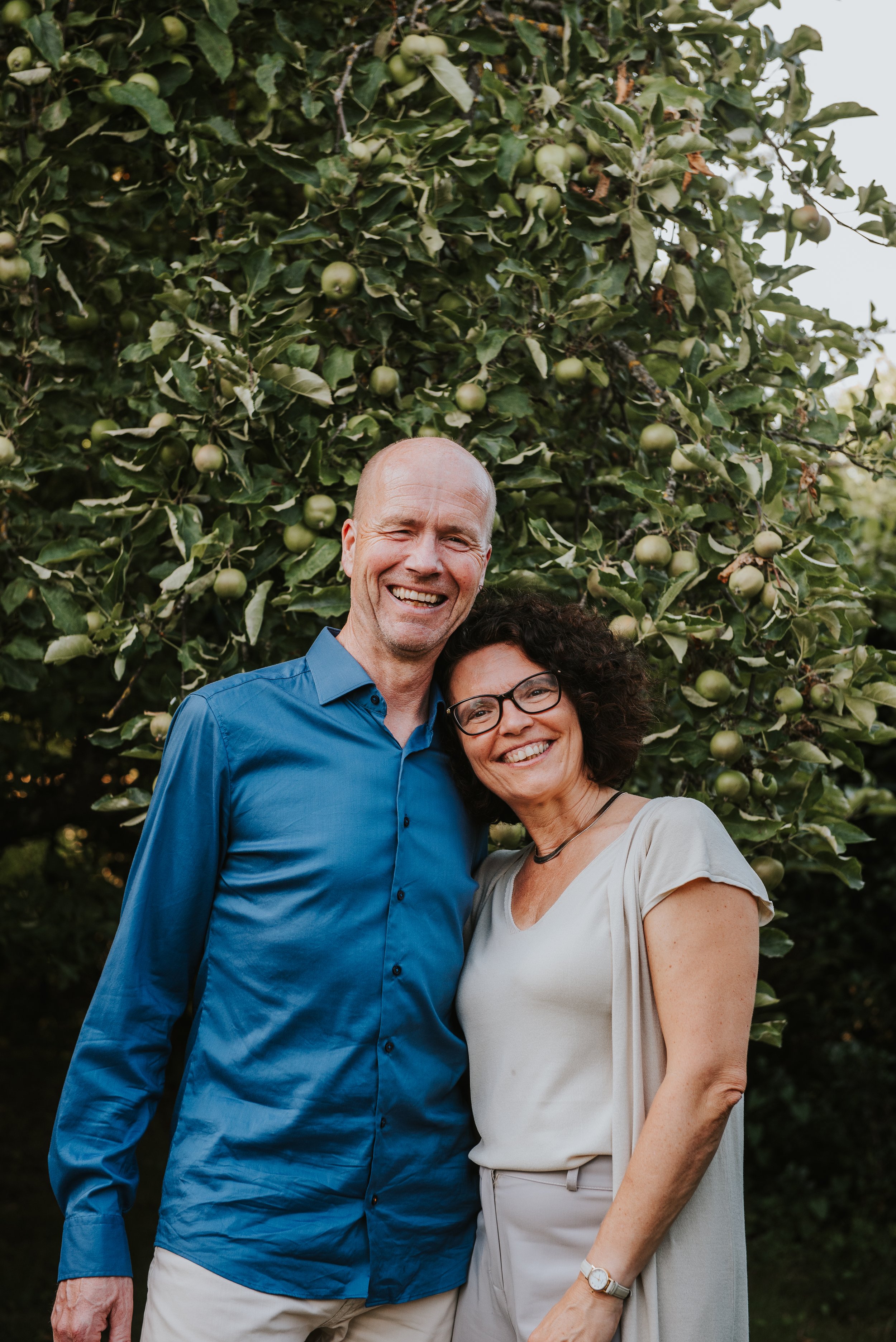 Twee mensen glimlachen en staan dicht bij elkaar voor een groene boom met groene appels.