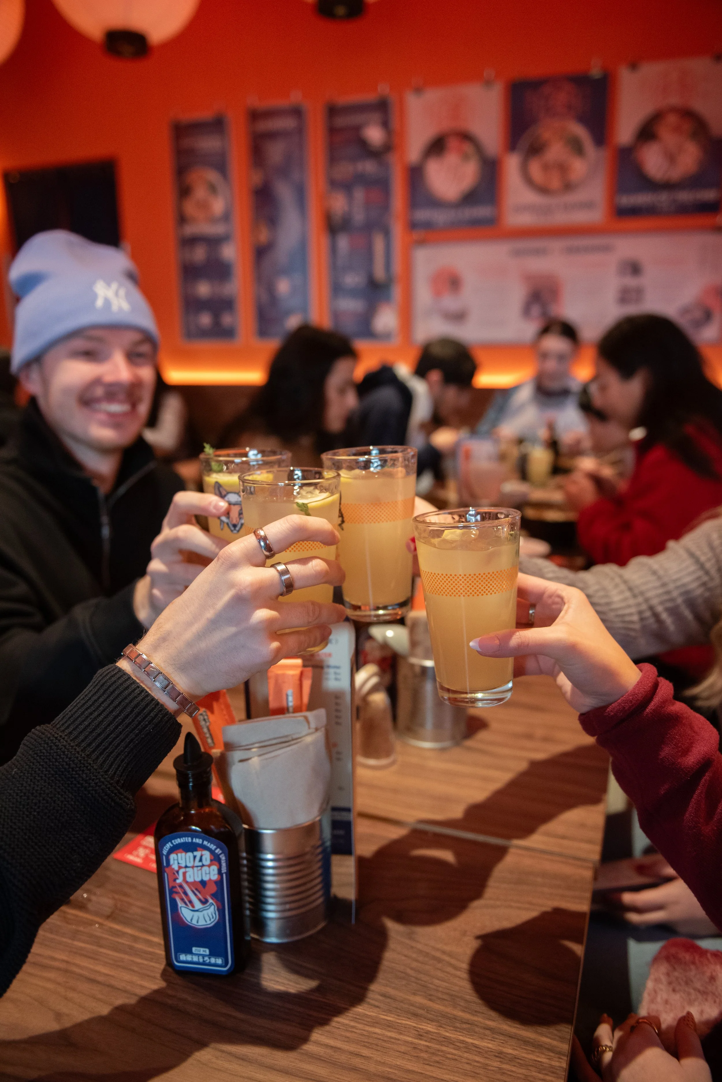 Mensen die in een restaurant een toast uitbrengen met lichte gele drankjes, met een ontspannen sfeer en kleurrijke decoratie op de muur.