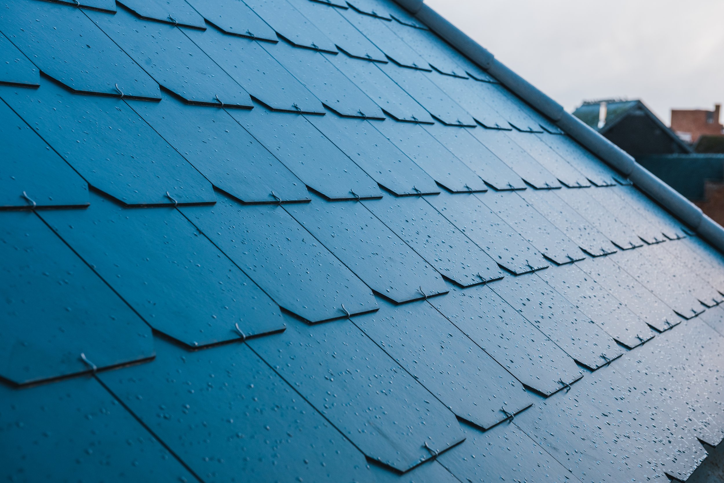 Blauwe dakpannen met waterdruppels in de regen.