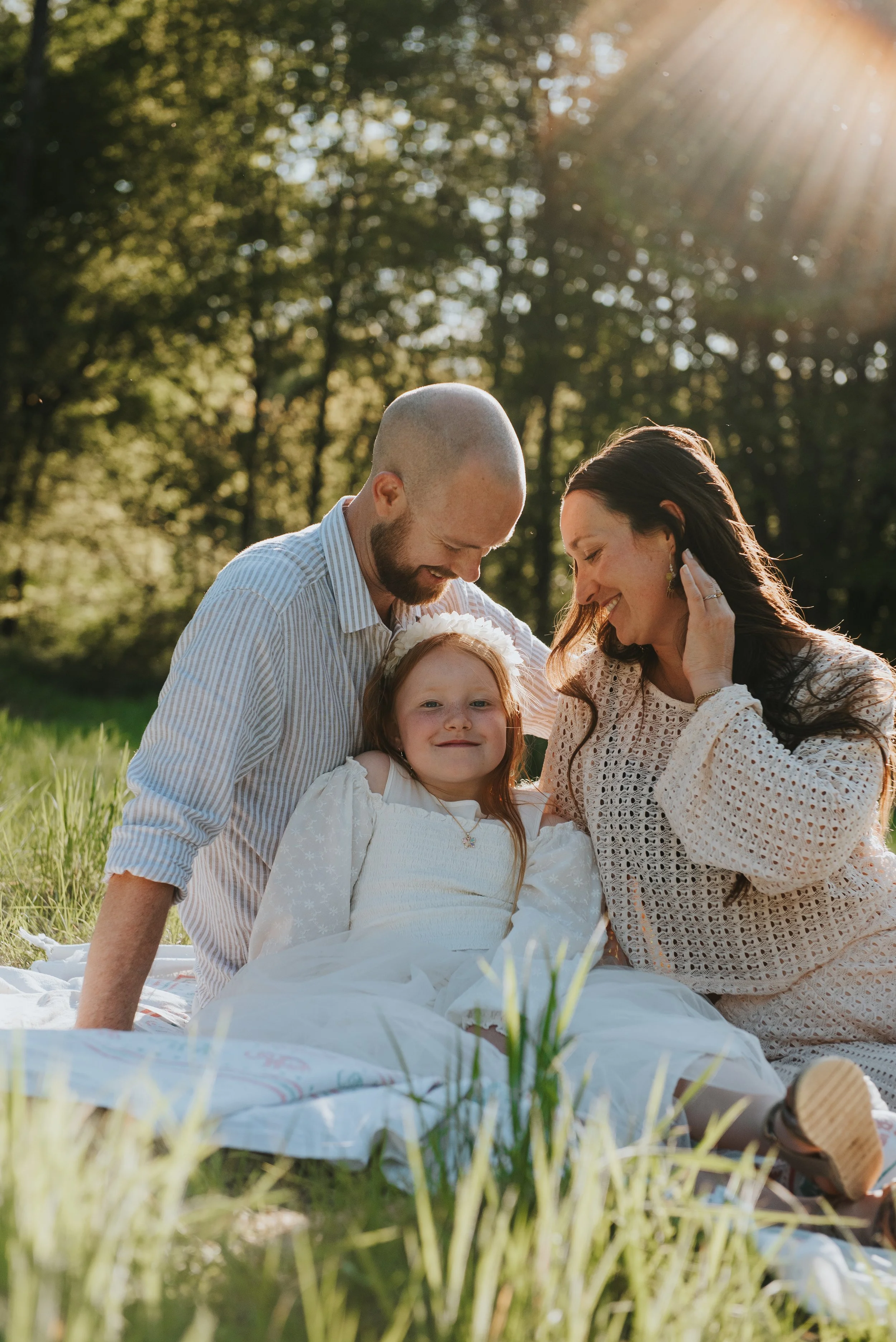 Een gezin zit samen op een grasveld in de natuur op een zonnige dag, lachend en genietend van elkaars gezelschap.