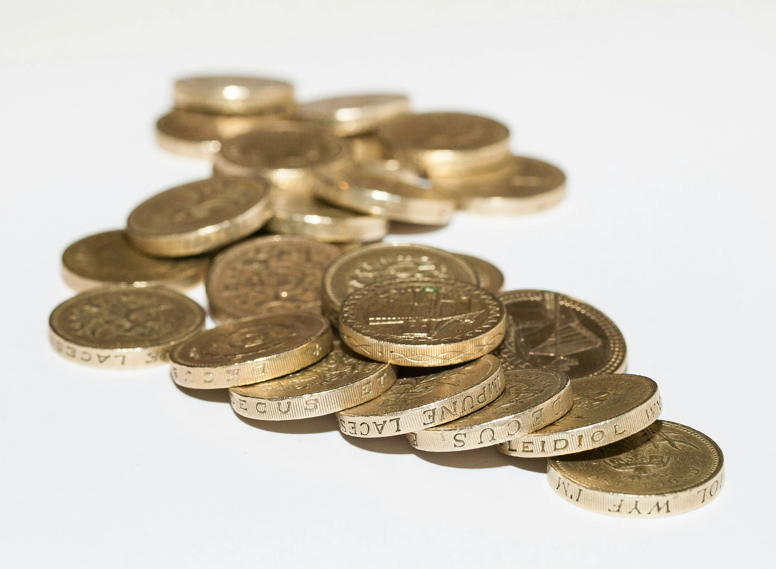 Pile of gold-colored coins scattered on a white surface.