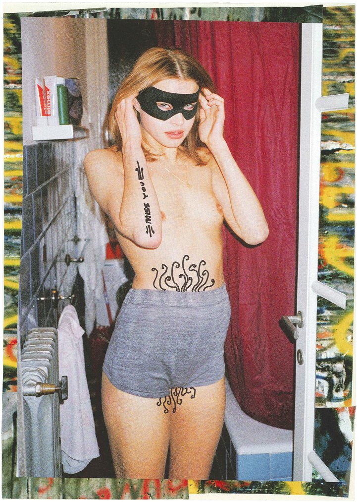 A woman with a black mask, tattoos, and grey shorts standing in a bathroom.