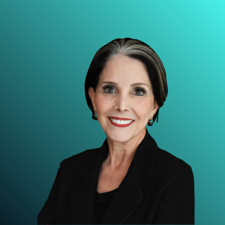 A professional woman with short dark hair streaked with gray, smiling, wearing a black blazer, and standing against a dark gray background.