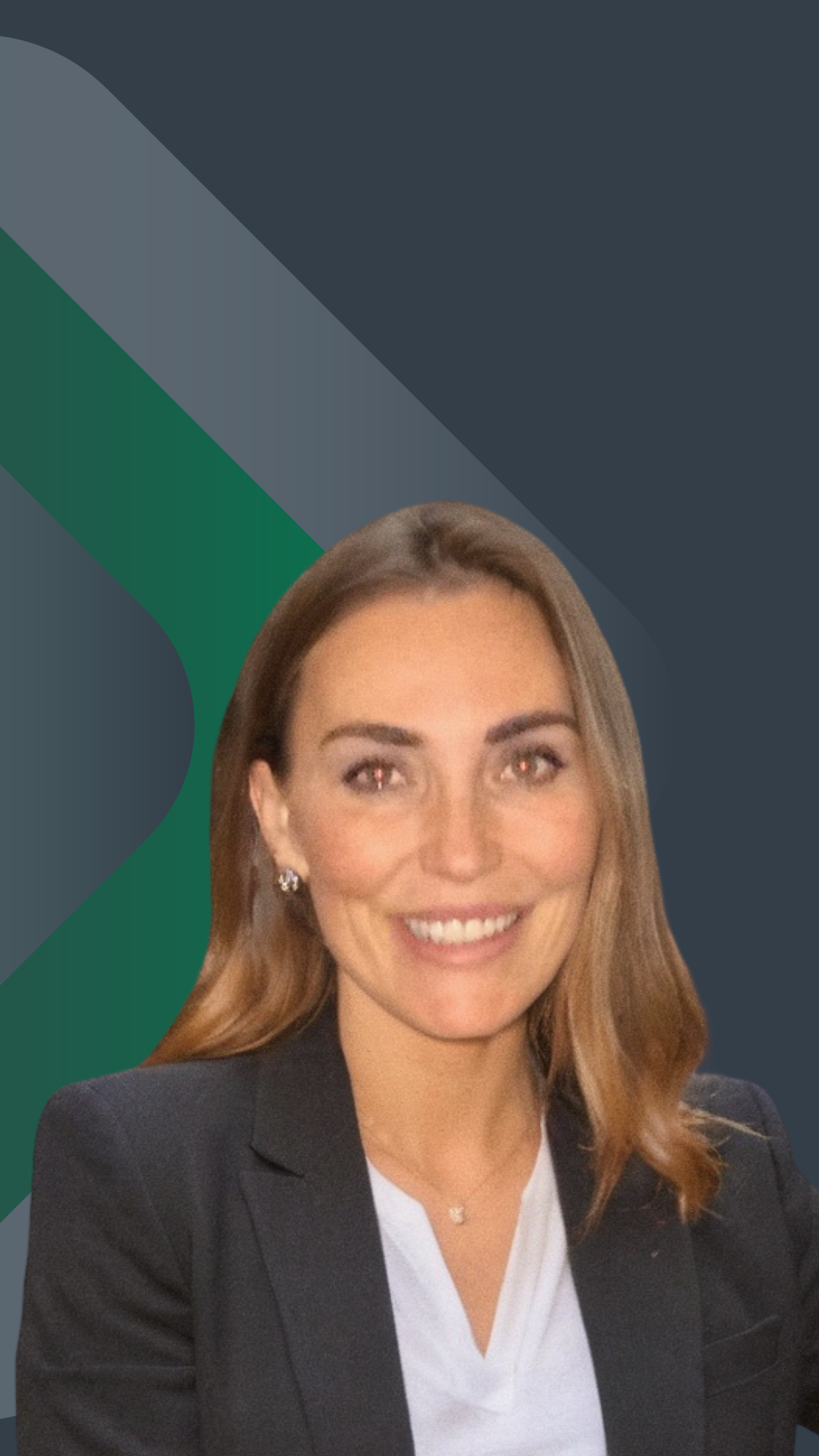 A smiling woman with long brown hair wearing a white long-sleeve top, standing against a plain beige wall.