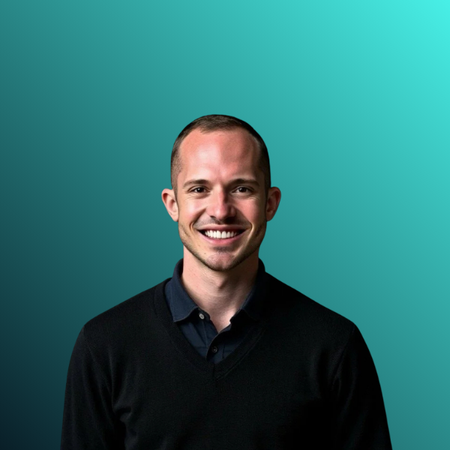 A smiling man with short hair wearing a dark sweater and dark collared shirt against a black background.