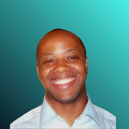 A smiling man with a shaved head wearing a light blue collared shirt.