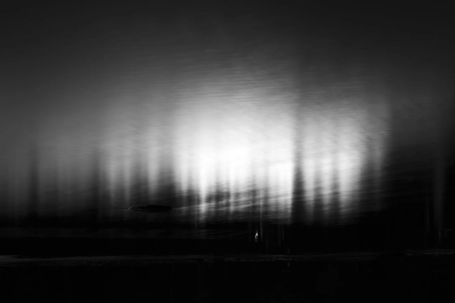 Black and white photograph of a blurred water scene with reflections and light patterns on the surface.