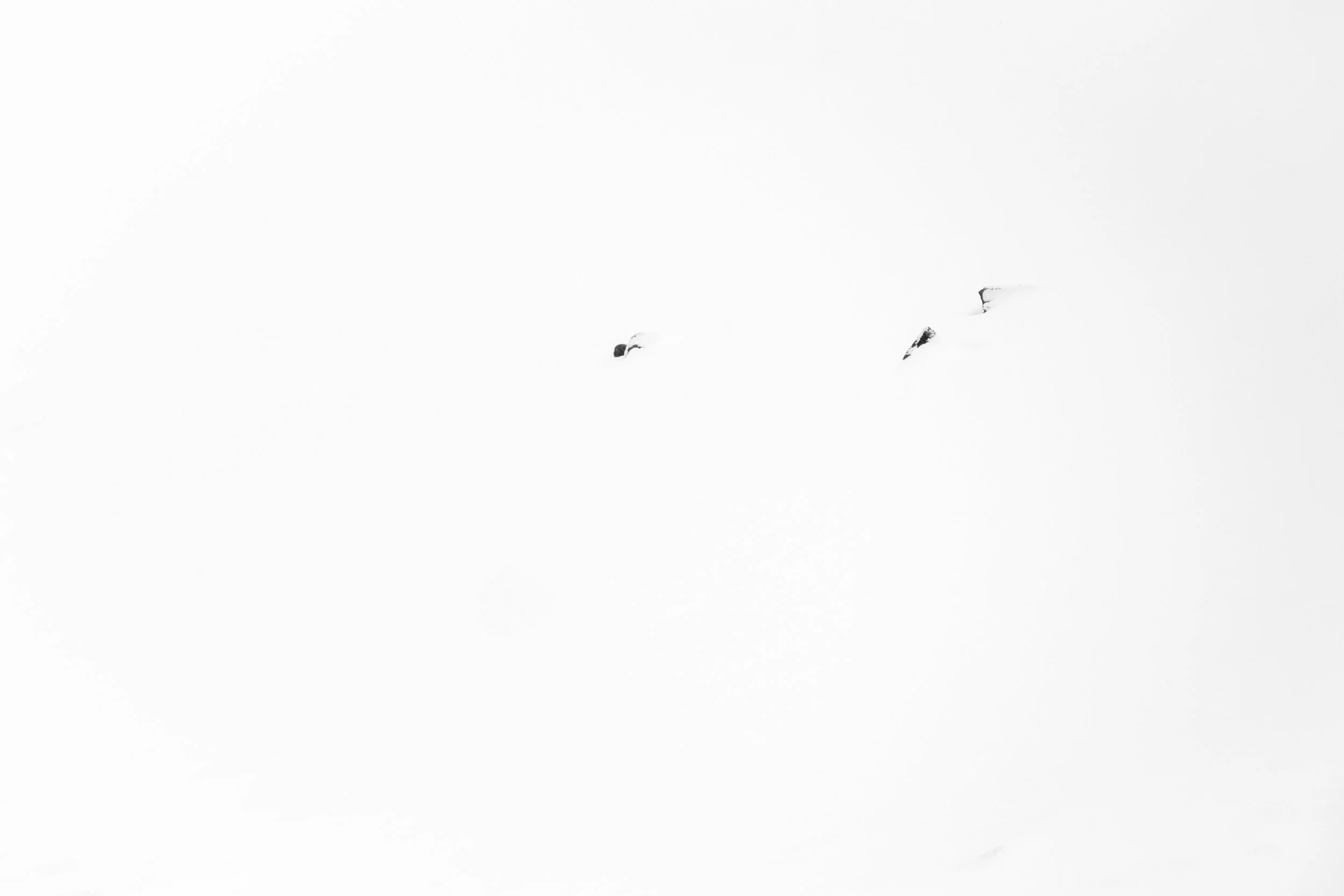 Snow-covered mountain landscape with three dark exposed rocks peeking through the snow.