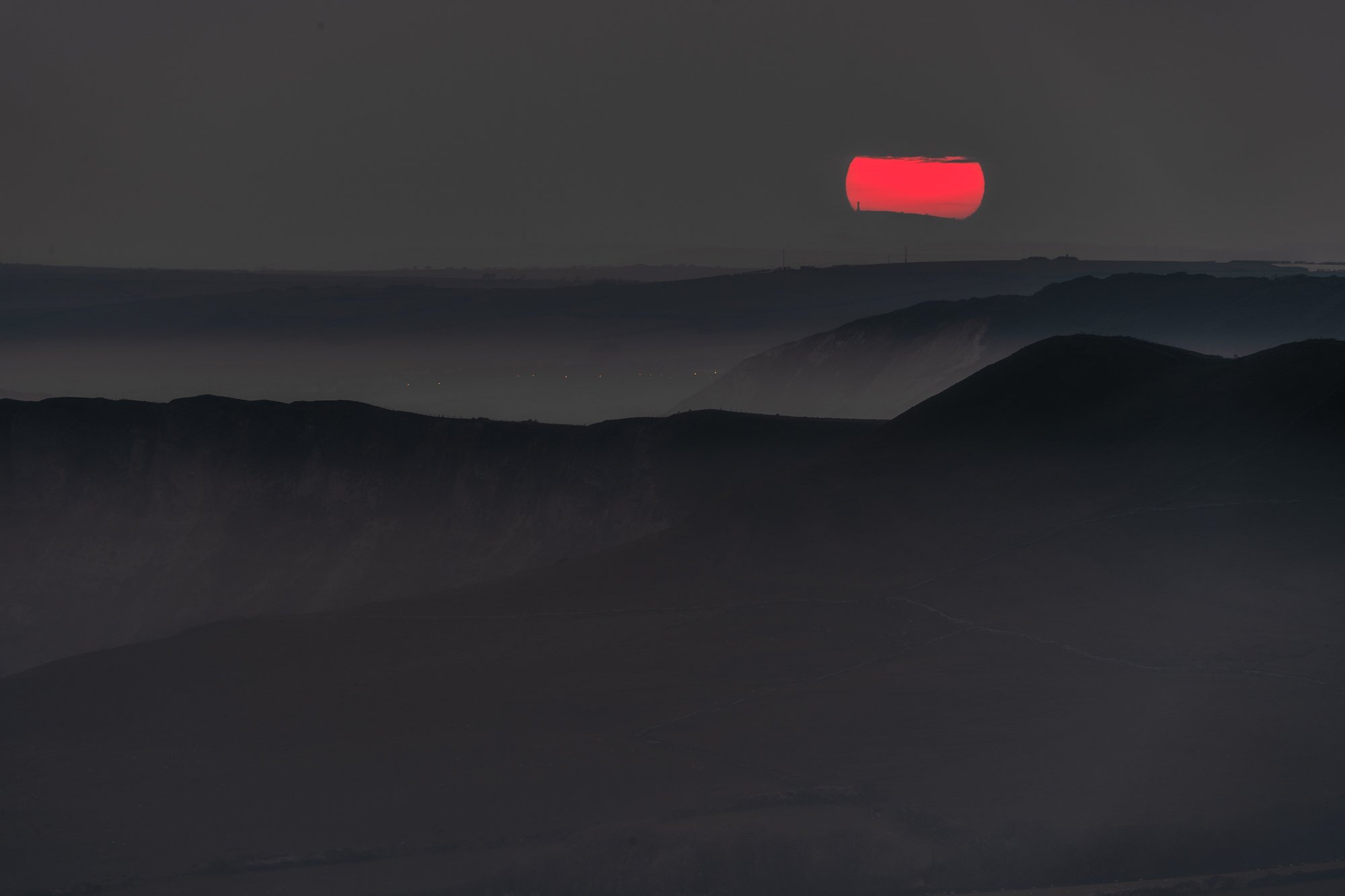 Sunset over mountainous landscape with dark cliffs and faintly visible valleys