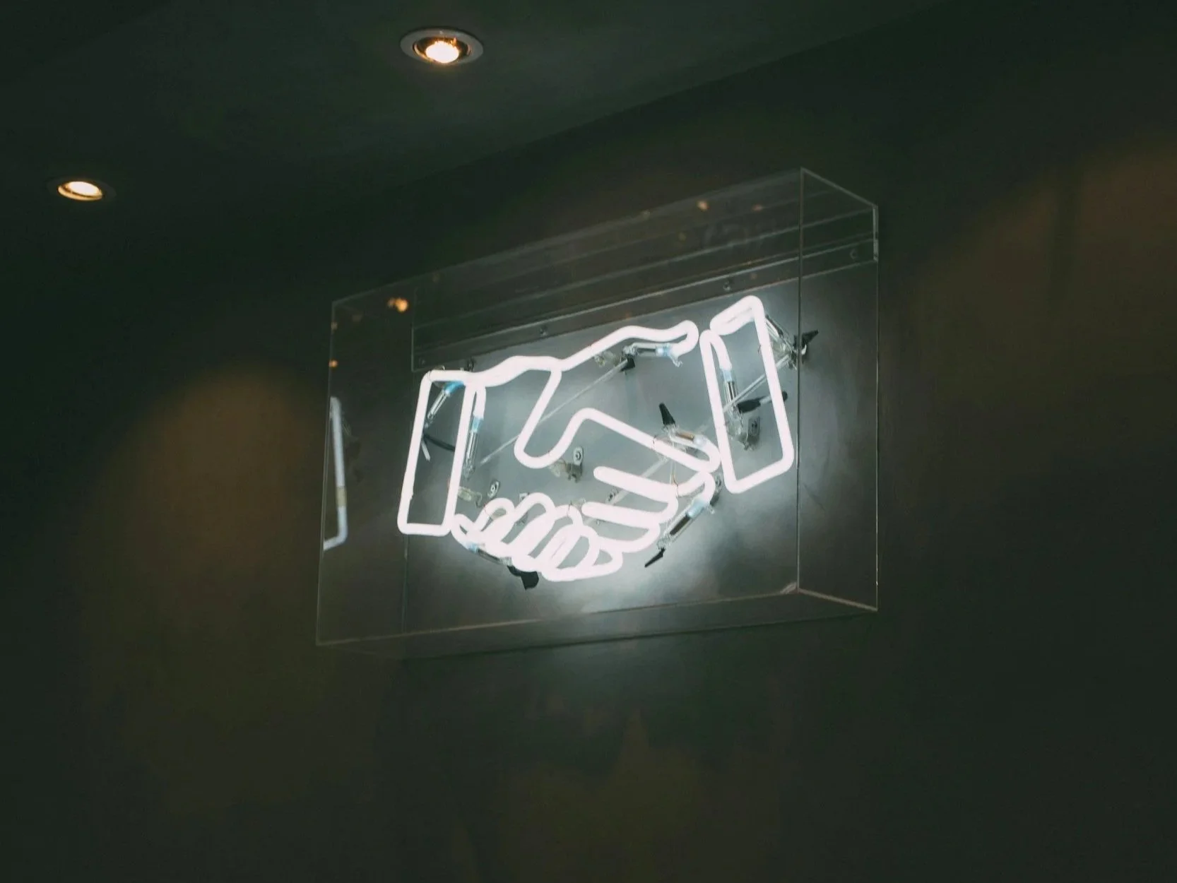 Neon sign of two shaking hands on a dark wall.