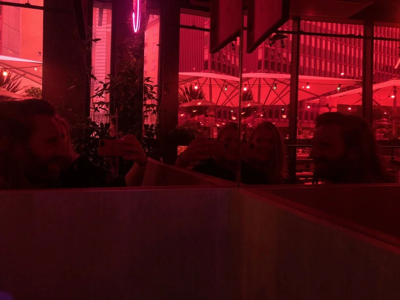 An abstracted photo washed in red. Two people look in a corner with two mirrors, so their images are repeated. Photo credit: Kelly Nielsen