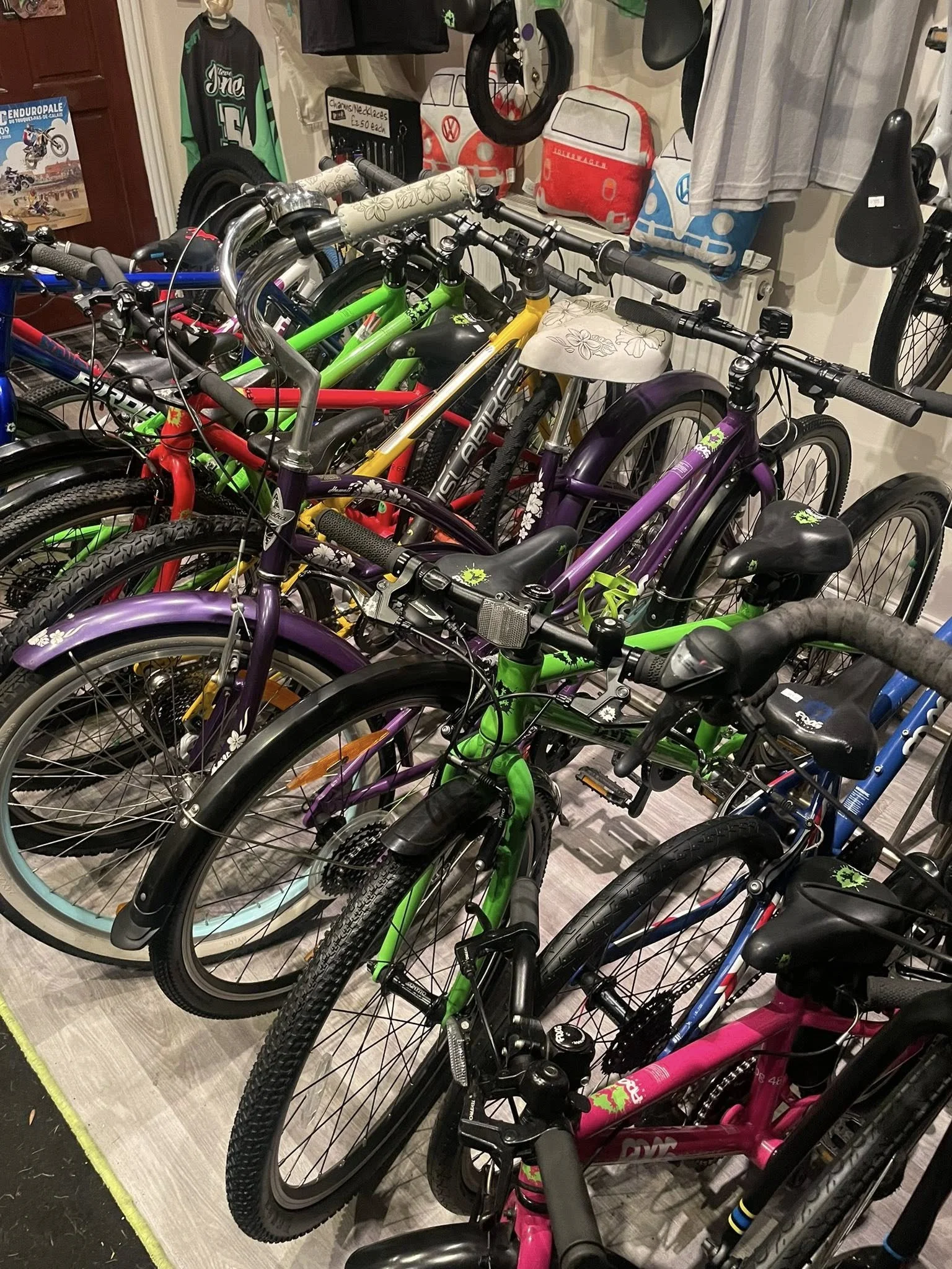 Multiple colorful bicycles parked indoors with display of bags and a bicycle on the wall.