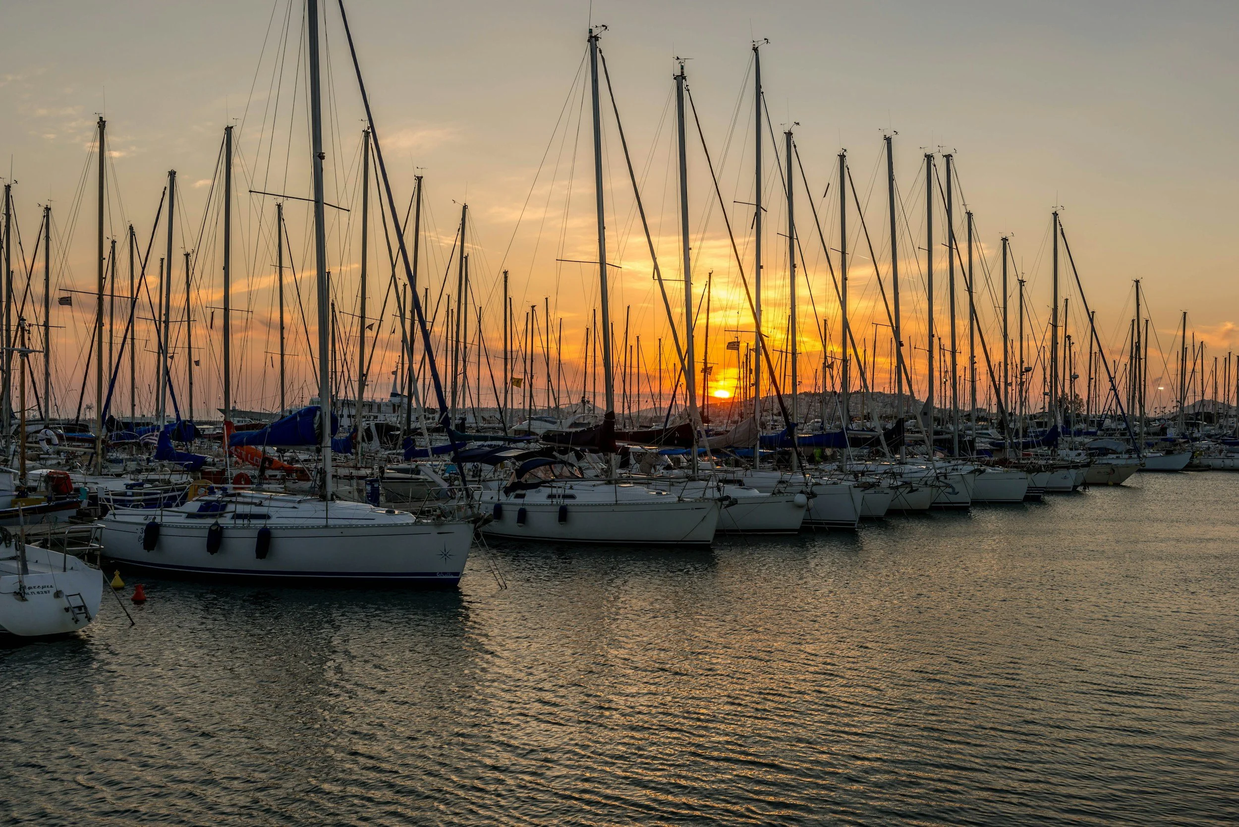 A marina at sunset filled with numerous docked sailboats and yachts.