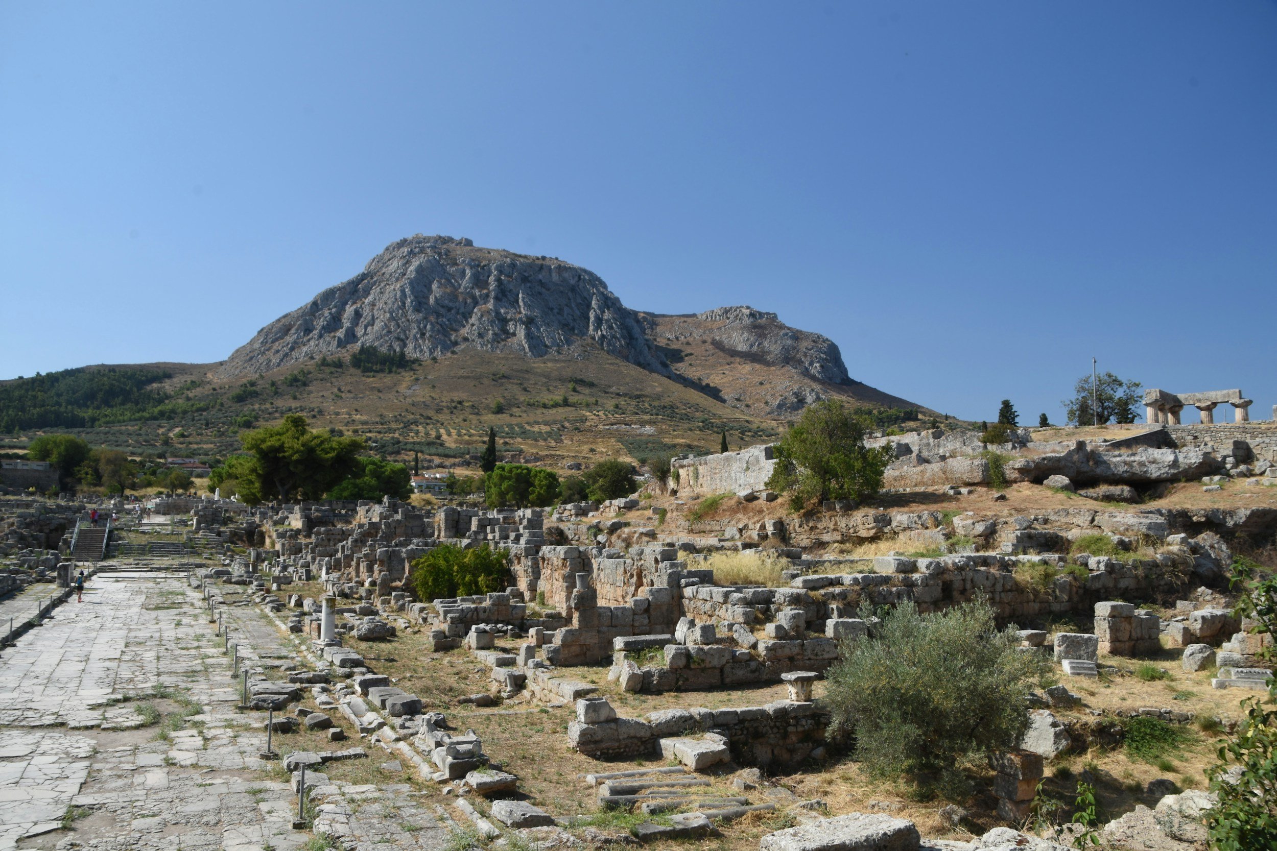 Ancient ruins with stone columns and steps, mountain in the background, and a clear blue sky.
