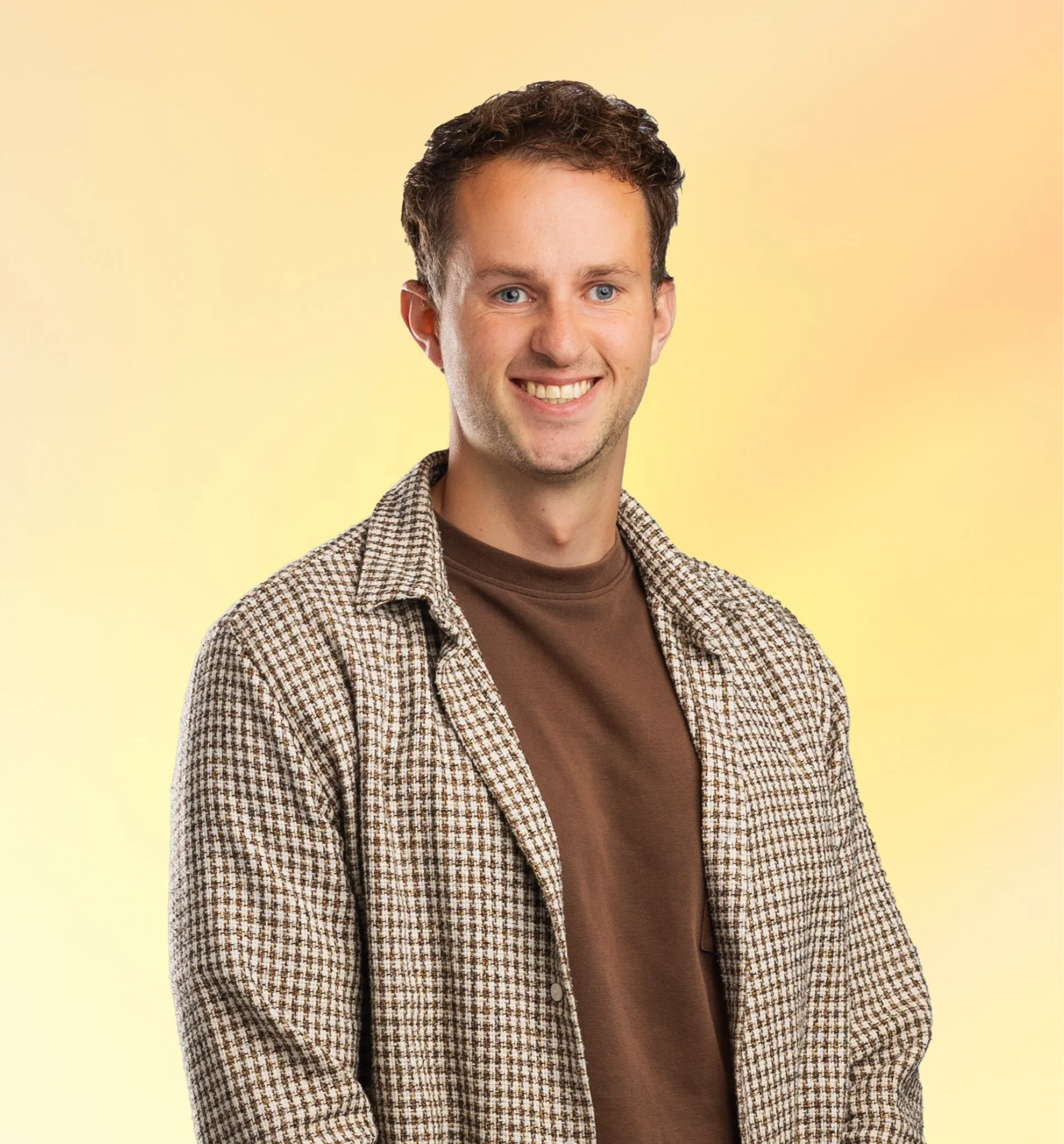 Portret van een jonge man met bruin haar en blauwe ogen, lachend, gekleed in een bruin T-shirt en een geel bruin geruit overhemd, met een gele achtergrond.