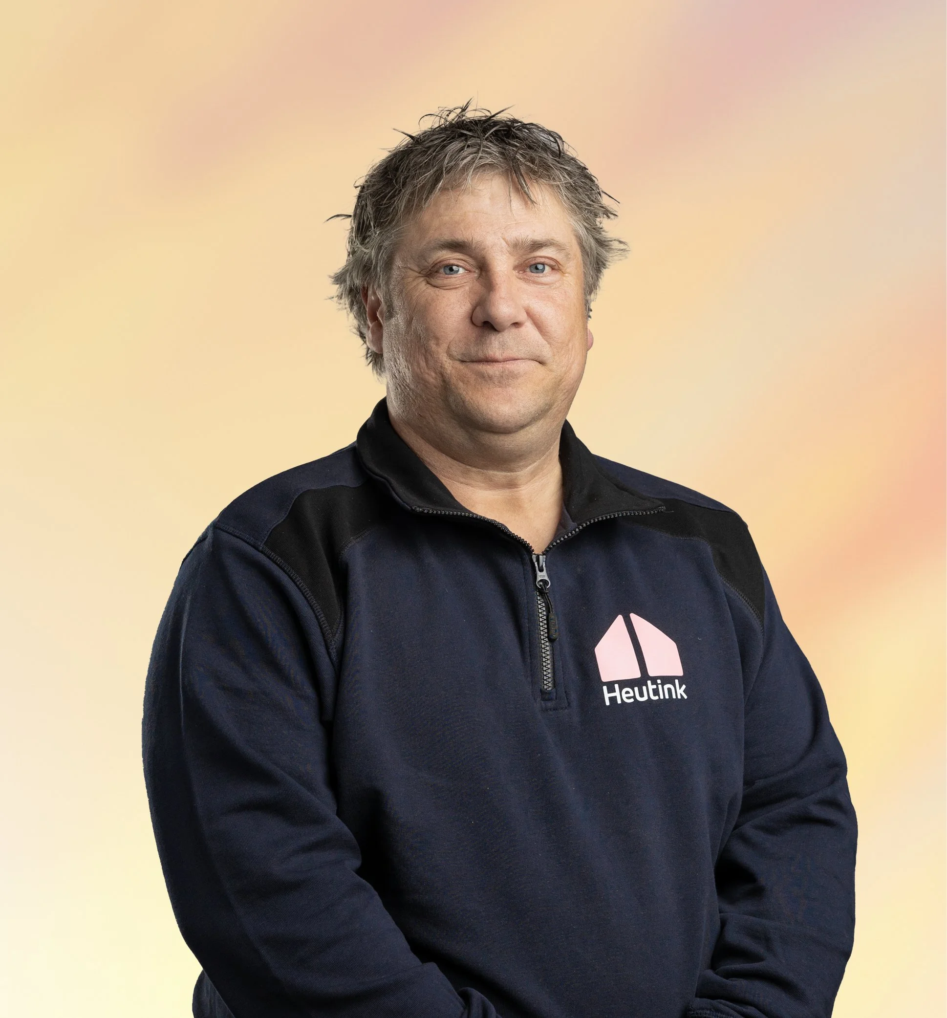 Man draagt een donkerblauw trui met een rits en een logo met de tekst 'Heutink'.