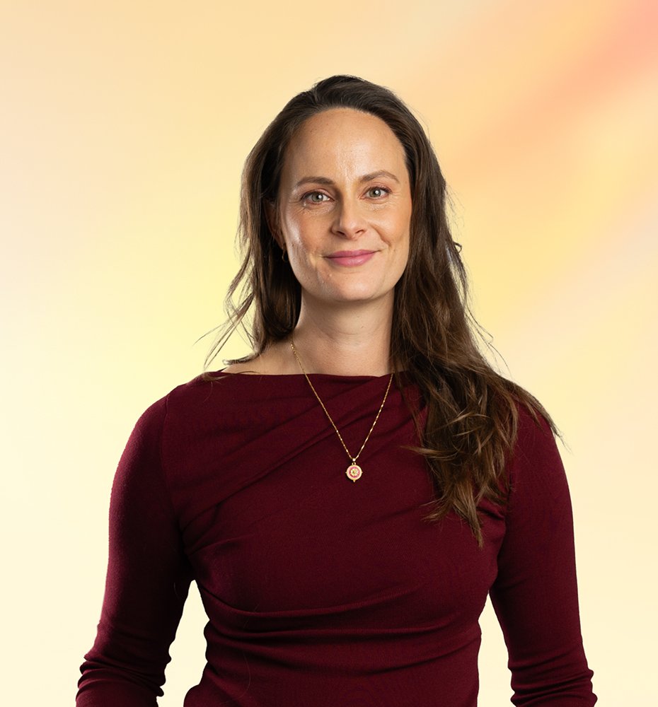 Portret van een vrouw met bruin haar en een bordeauxrode jurk, lachend, met een kleurrijke zachte achtergrond.