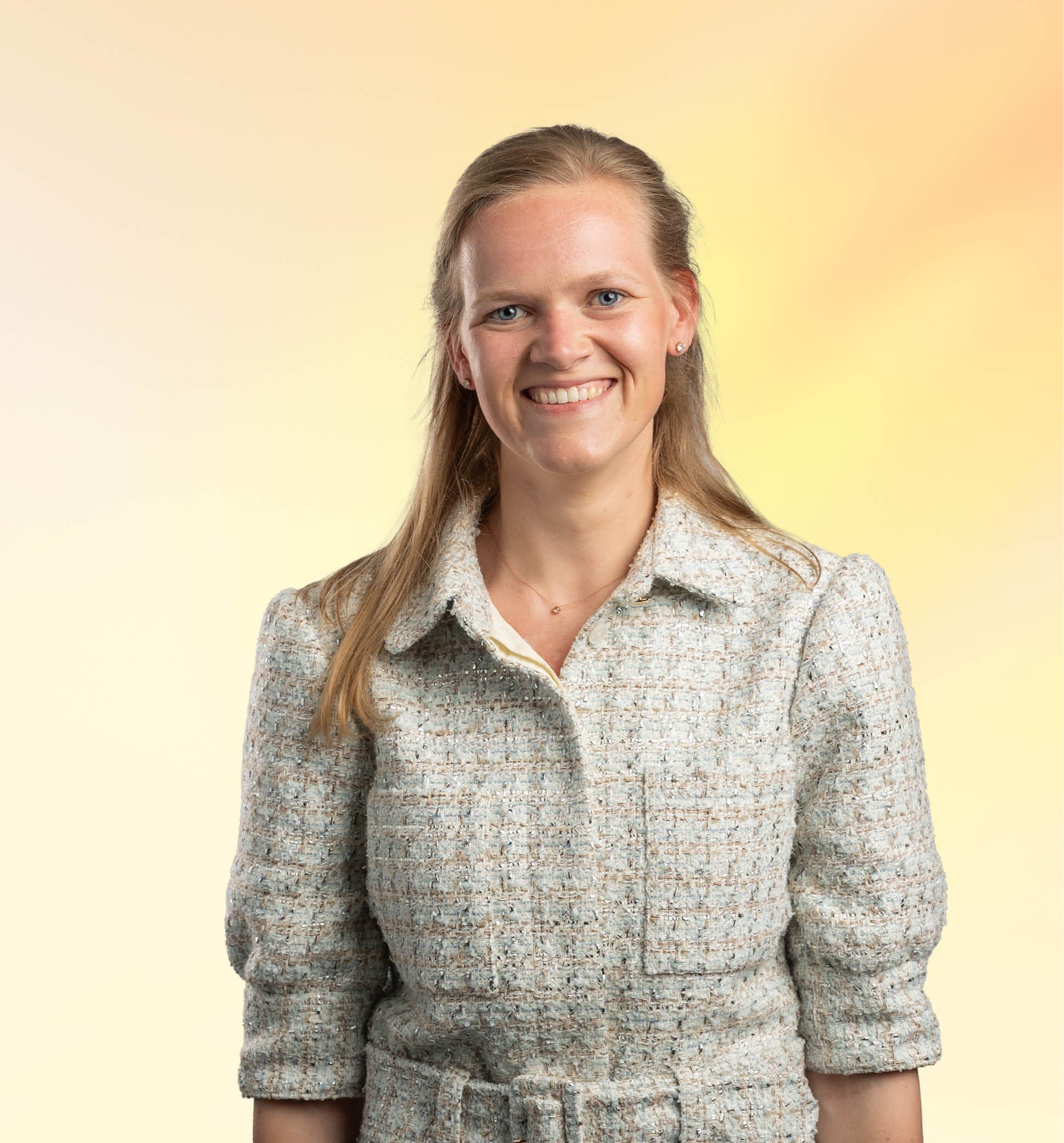 Portret van een lachende vrouw met lang, lichtbruin haar, gekleed in een gebreide sweater, tegen een gele en oranje achtergrond.