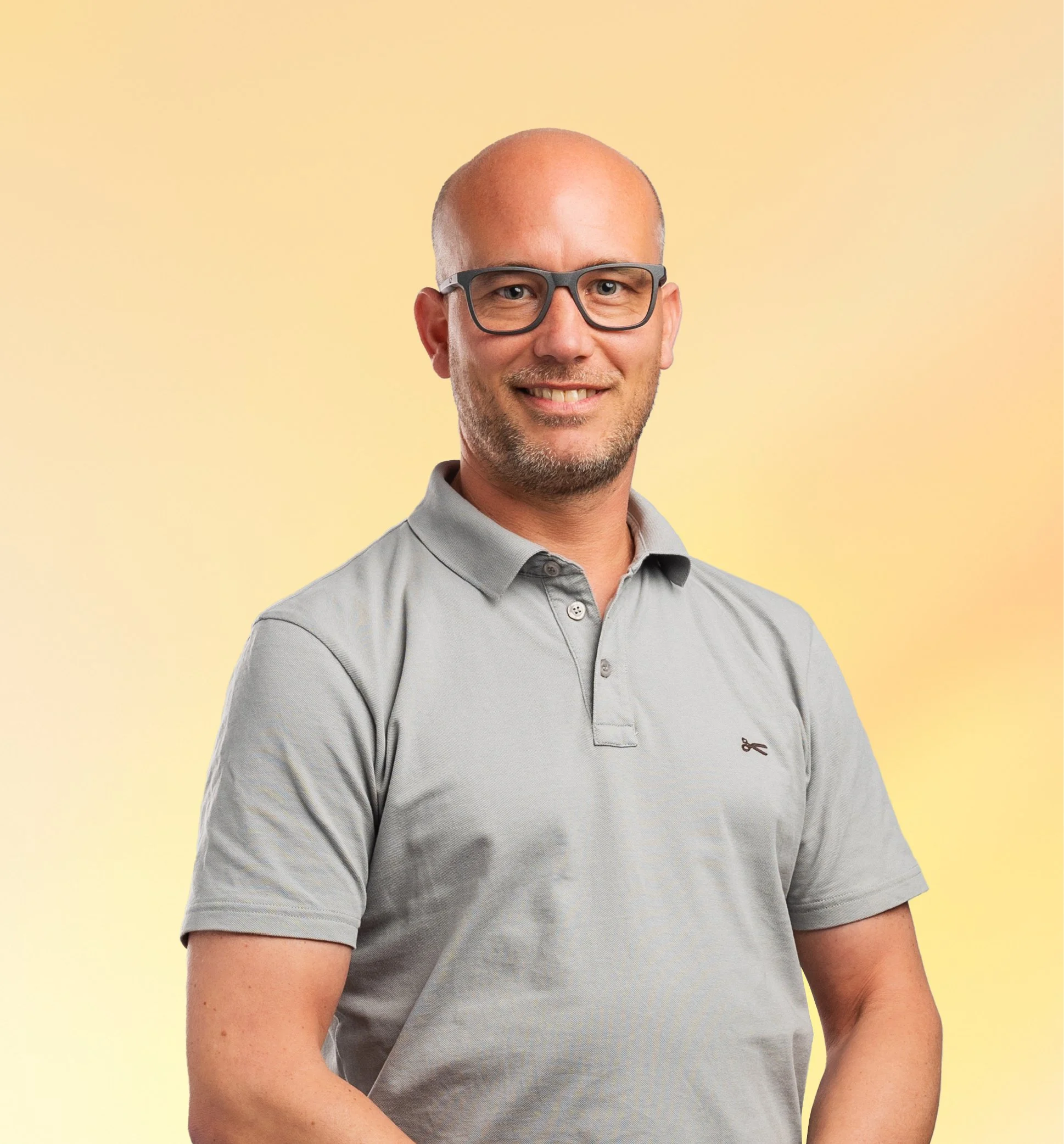 Man met glazen, grijze polo, glimlacht, op een geel-oranje achtergrond.