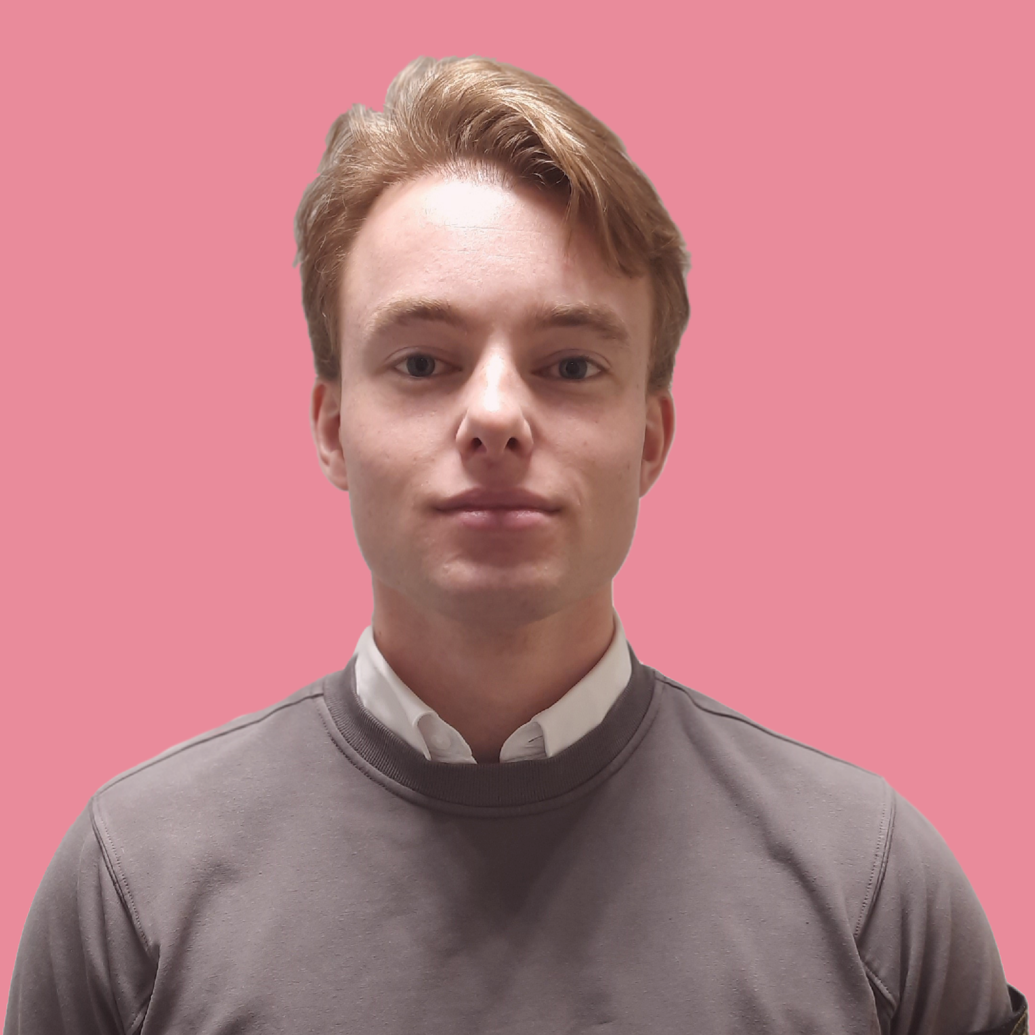 Portret van een jonge man met lichtbruin haar, gekleed in een grijs sweatshirt en een witte blouse, staand voor een effen roze achtergrond.
