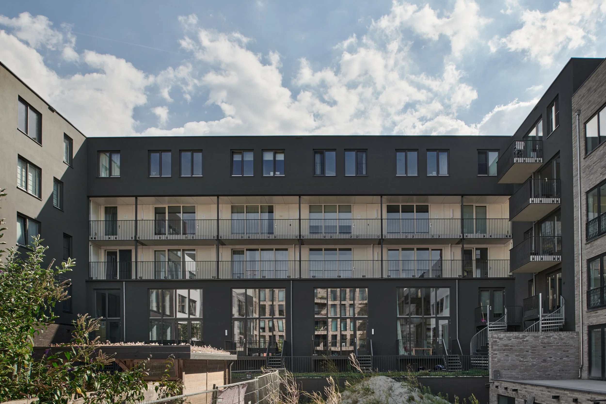 Moderne vier verdiepingen tellende appartementencomplex met grote ramen en balkons, tegen een blauwe hemel met wolken.