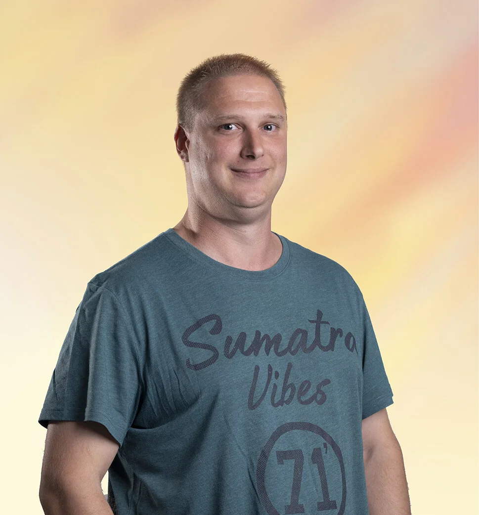 Een glimlachende man met blond haar en een blauwe T-shirt met de tekst 'Sumatra Vibes' voor een kleurrijke achtergrond.