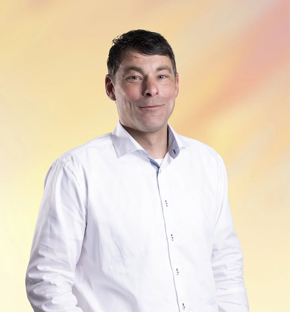 Man met donkere haar in een witte blouse, lachend, voor een kleurrijke achtergrond