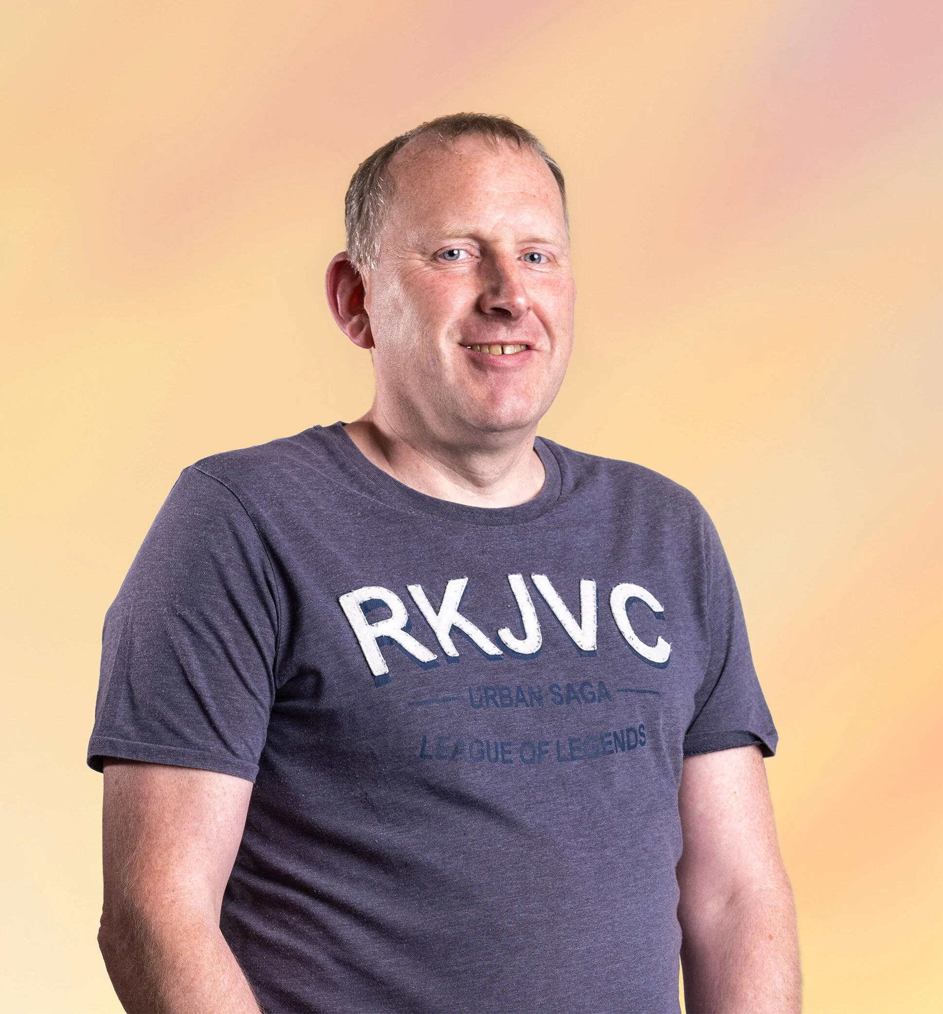 Man met korte haar in een grijs T-shirt met tekst, lachend, op een symbolische pastelachtergrond.
