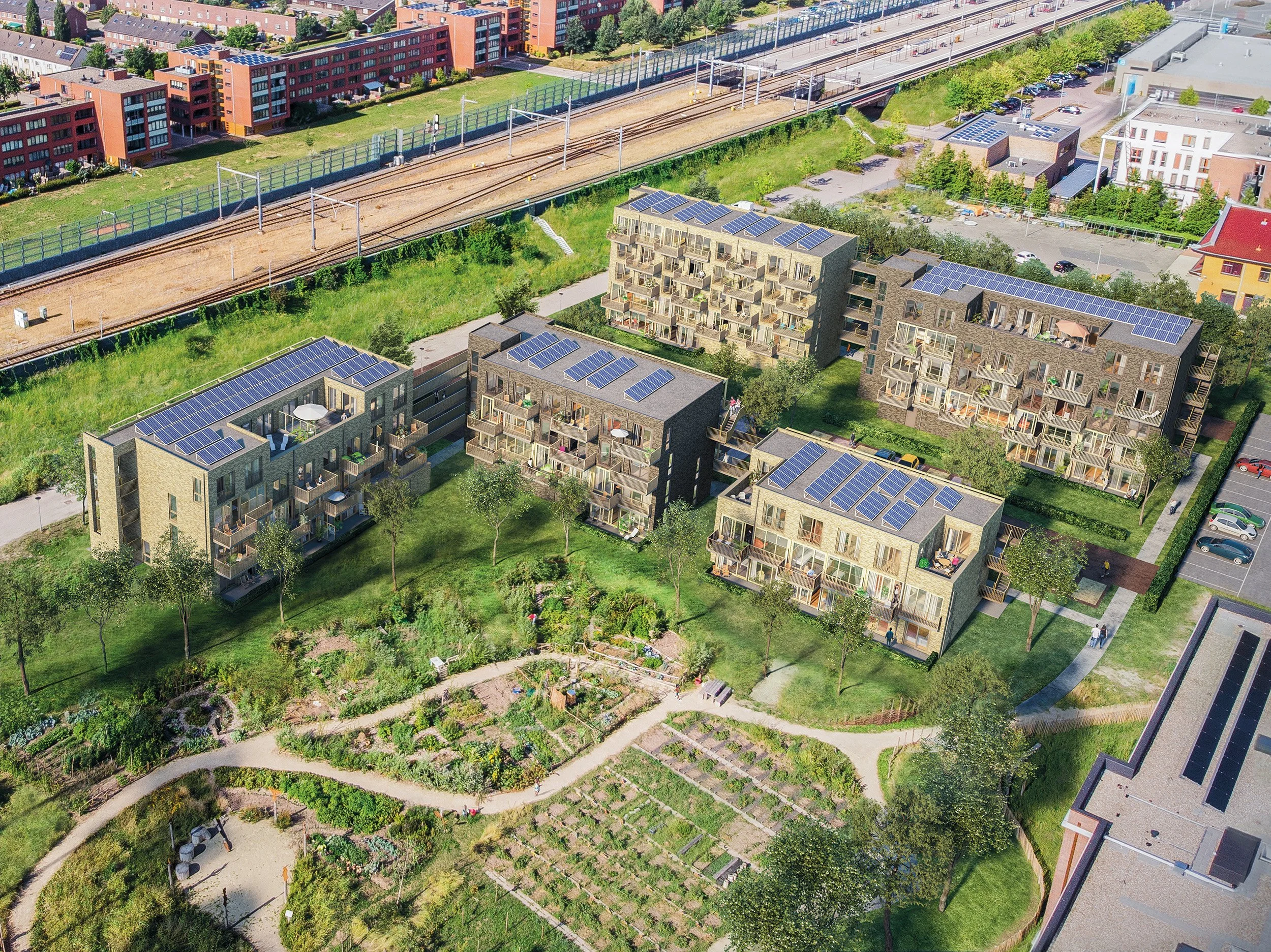 Een wijk met moderne appartementen met zonnepanelen op het dak, omgeven door groen en tuinen, met een spoorlijn op de achtergrond.