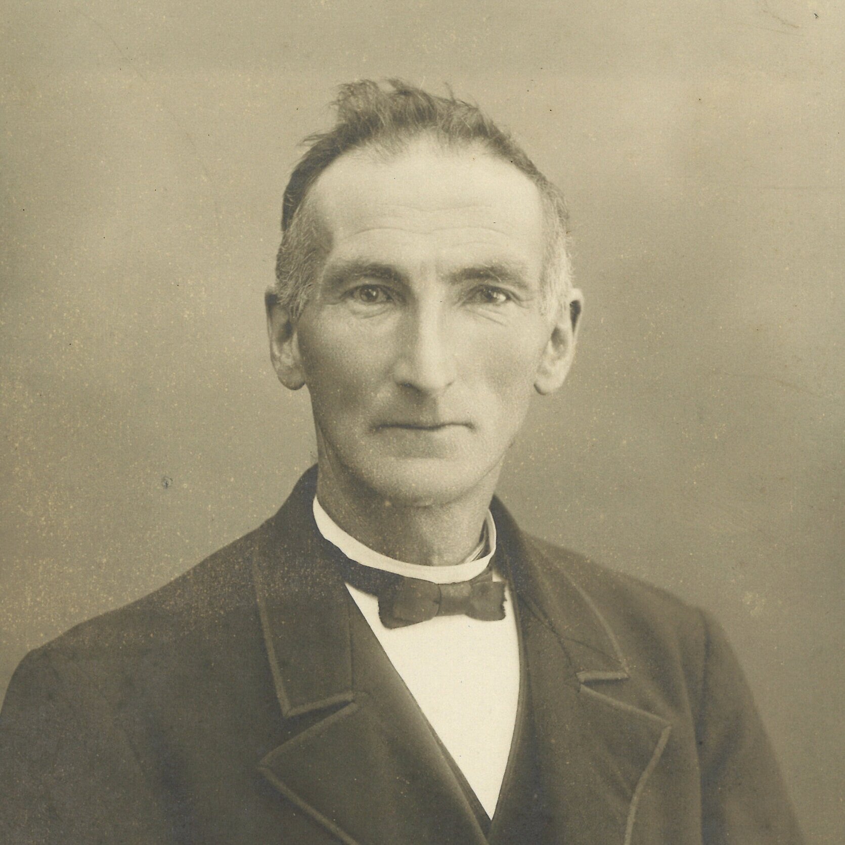 Zwart-wit foto van een man met een strakke blik, zwart pak en een vlinderdas, vermoedelijk uit de 19e of vroege 20e eeuw.