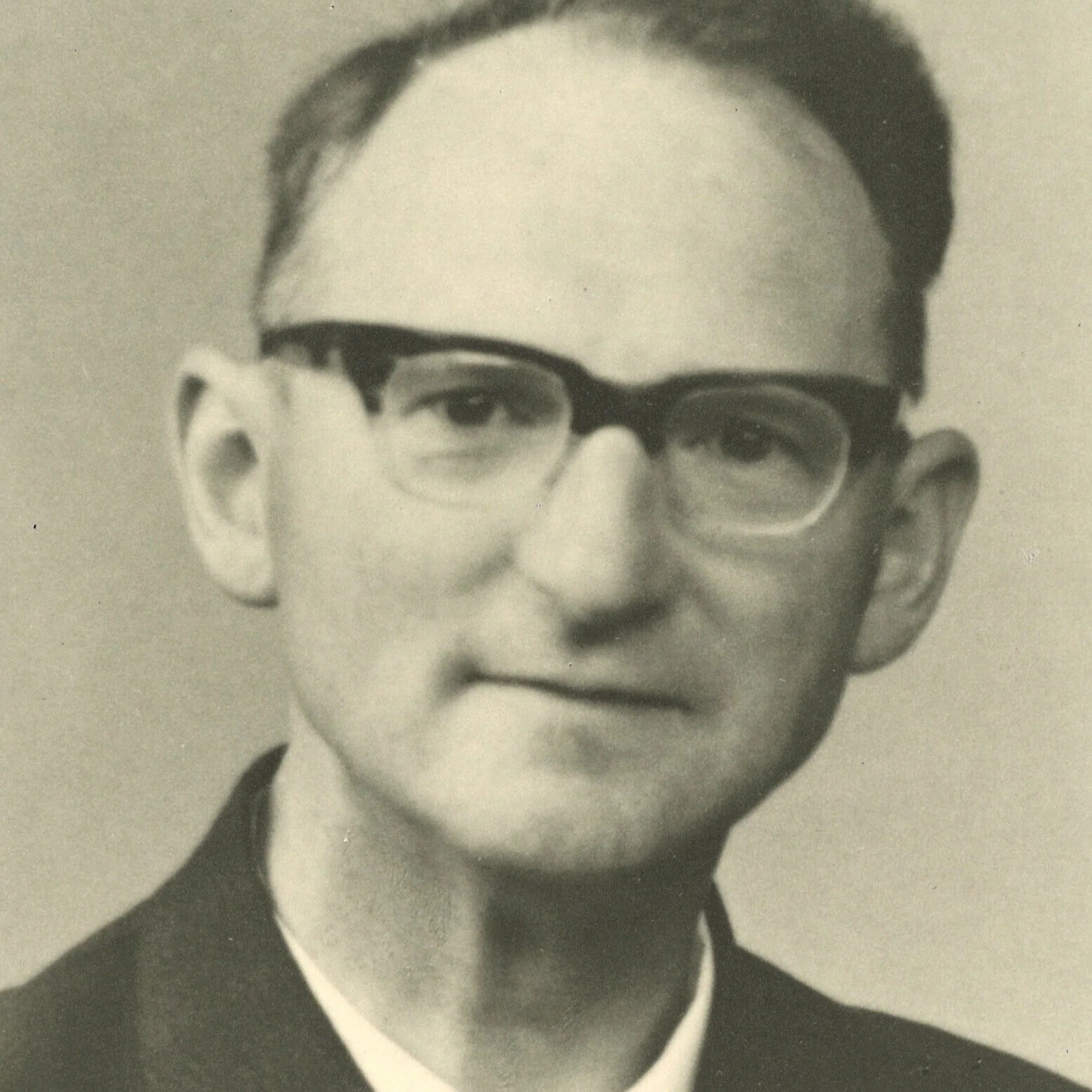 Zwart-wit foto van een man met bril, recht in de camera kijkend, gekleed in formele kleding.