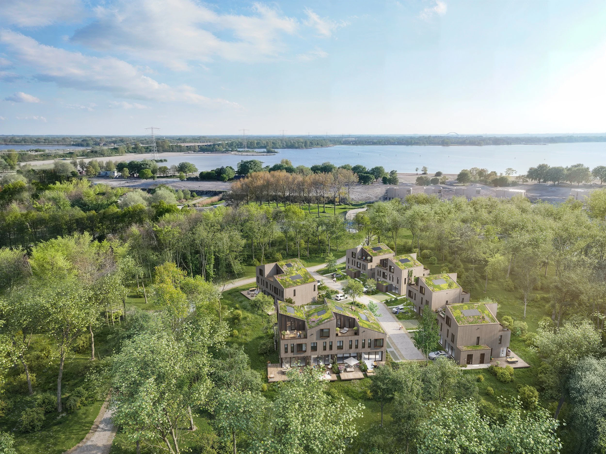 Luchtfoto van een modern woningcomplex omringd door veel groen, met een rivier op de achtergrond onder een deels bewolkte hemel.