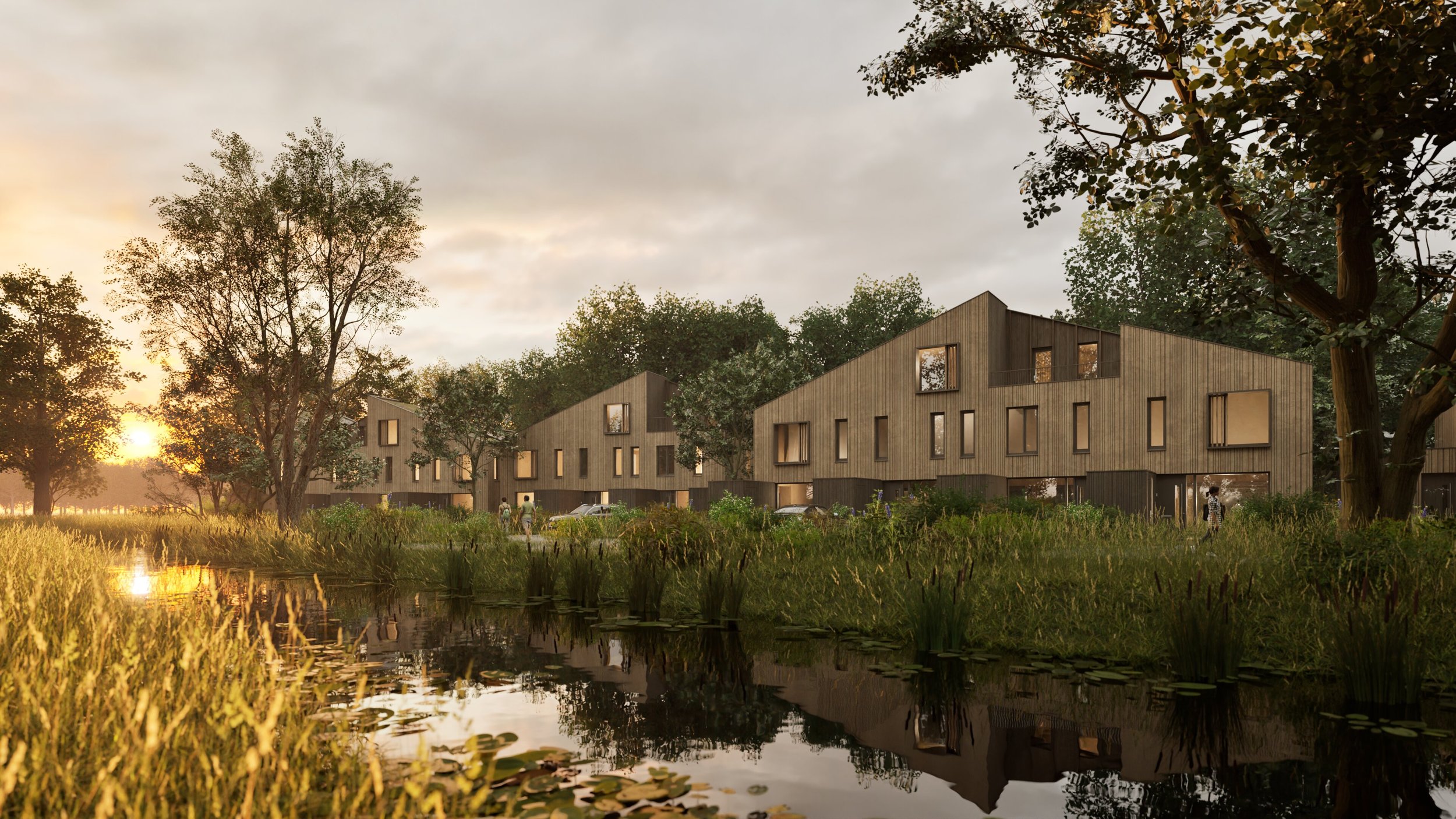 Moderne houten woningen aan een vijver tijdens zonsondergang, omgeven door bomen en gras.