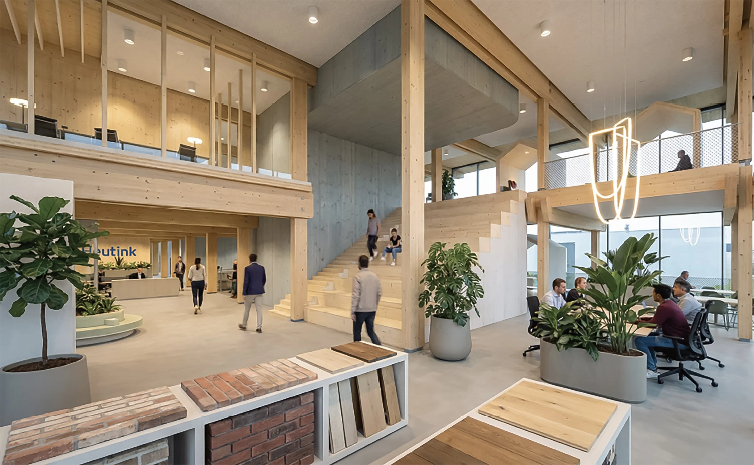 Interieur van een modern kantoorpand met veel hout, planten en een open indeling, inclusief trappen, werkplekken en wachtende mensen.