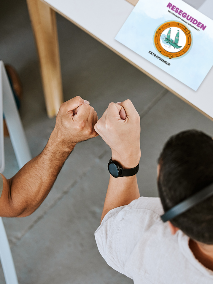 Two people with clenched fists bumping in a gesture of friendship or strength, seen from above near a white table with a book on it.